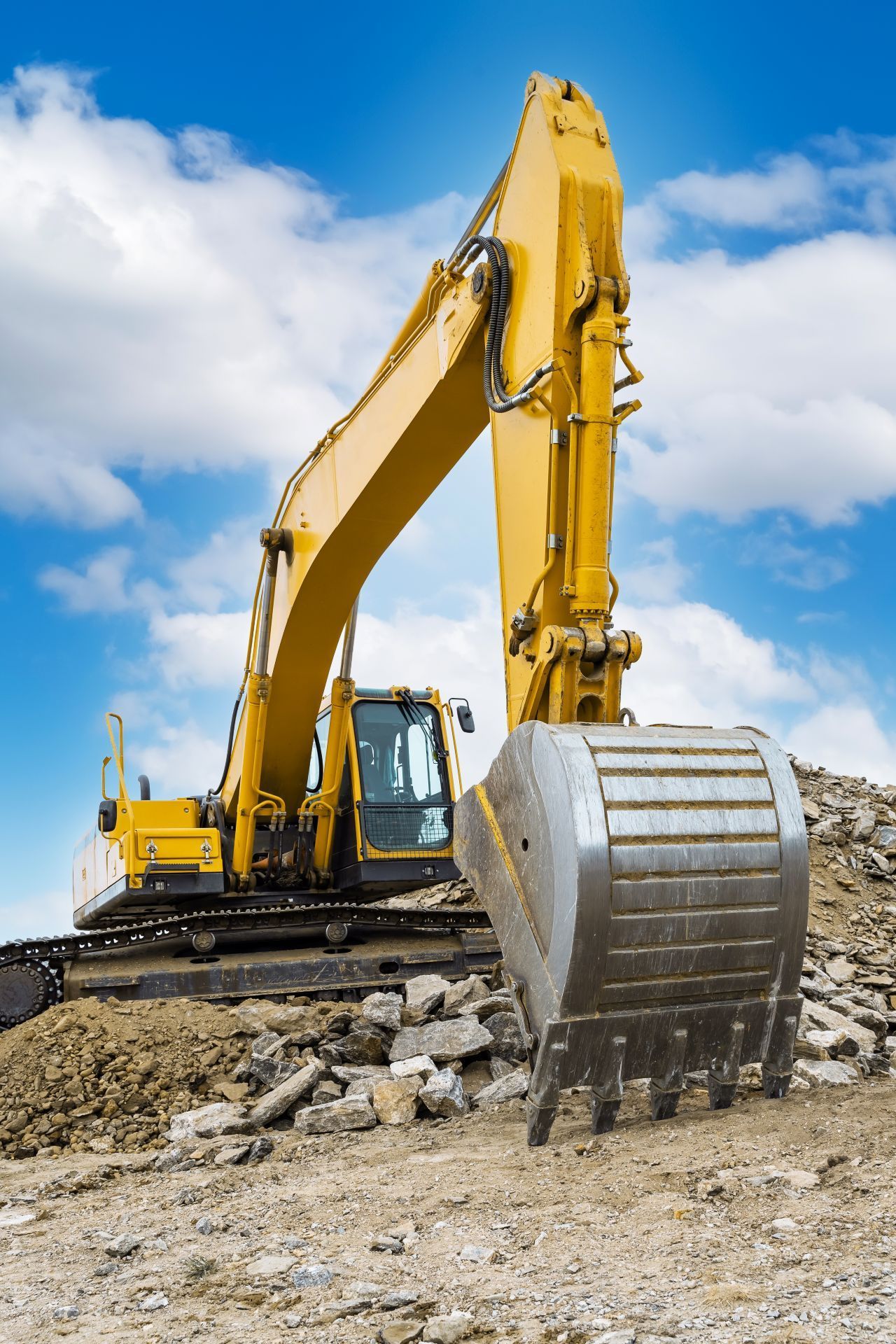 Yellow excavator with raised bucket on a construction site under a blue sky