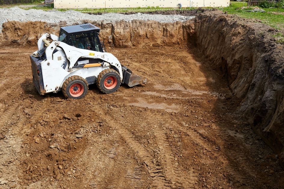 White skid-steer loader working in a large dirt excavation pit