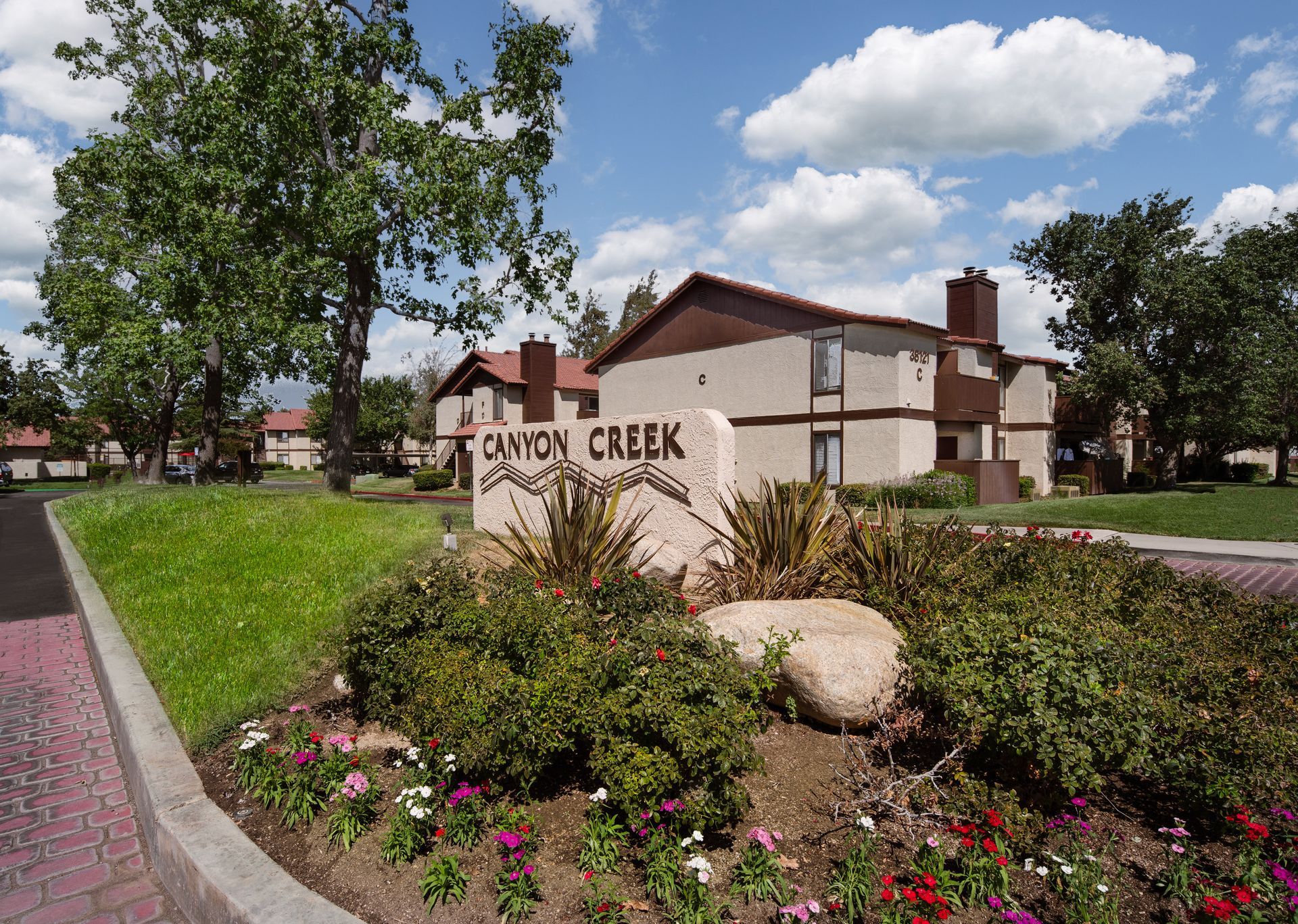 Canyon Creek apartment complex entrance sign, with buildings, greenery, and a cloudy sky.