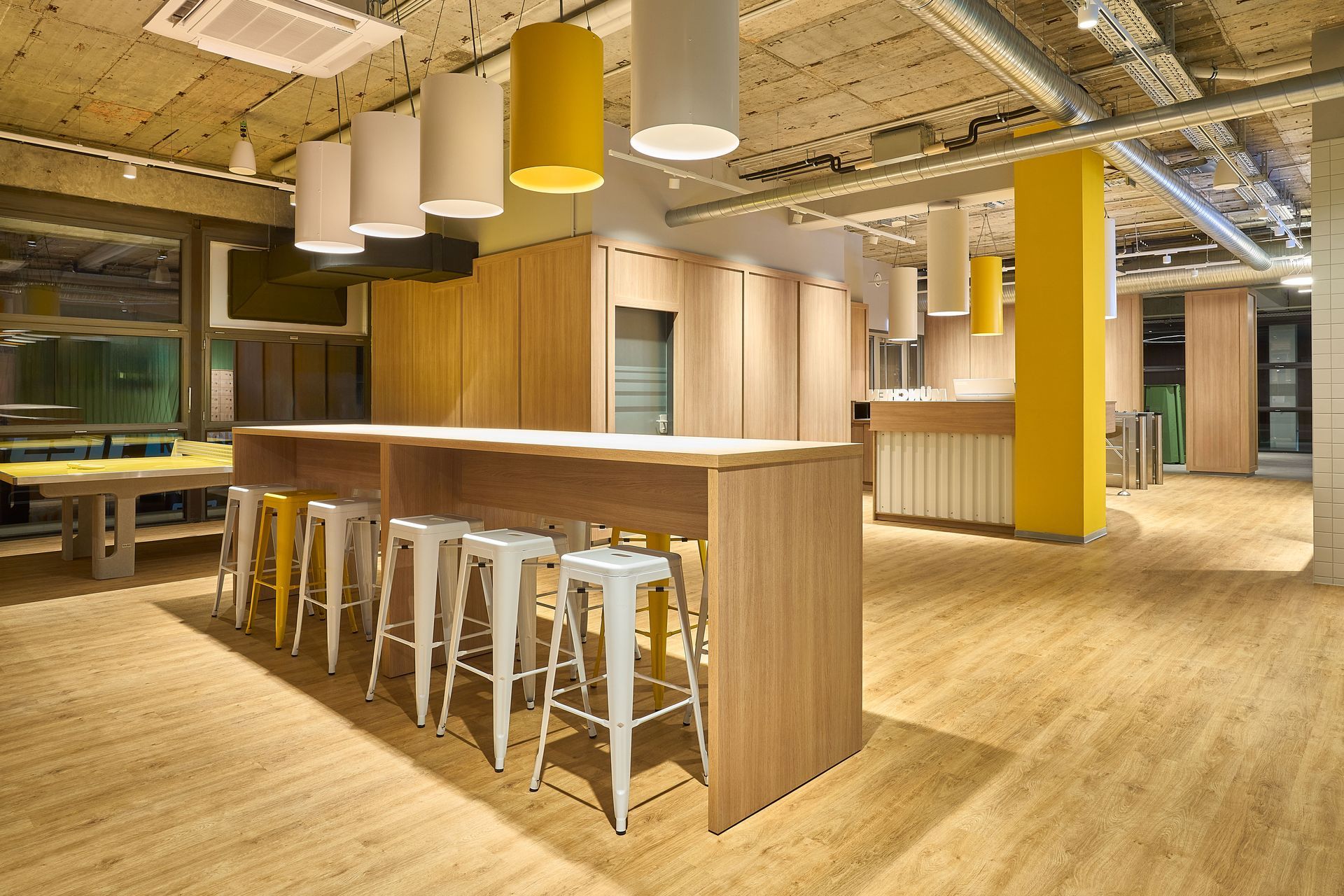 Innenausbau Fitnessstudio McFIT München Forstenried - Eingangsbereich moderne Lounge im Innenausbau mit hoher Bartheke, gelben Hockern, stylischen Deckenlampen - Referenzprojekt Fitnessstudio Innenausbau Generalunternehmer