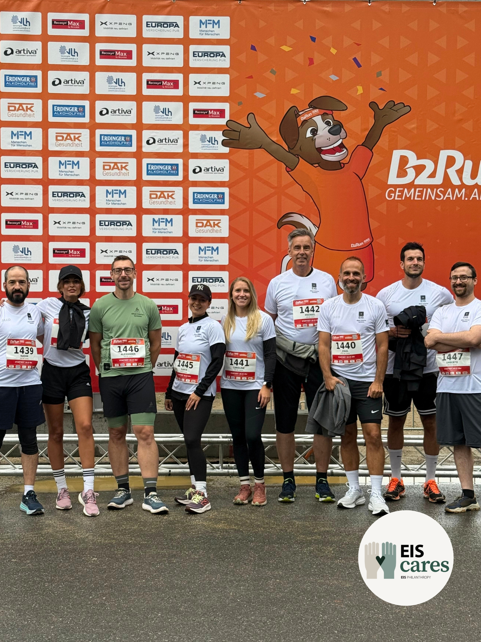 Teamaufstellung des Generalunternehmes aus Aschaffenburg für die Teilnahme am B2Run Frankfurt Firmenlauf für soziales Engangement. Unsere Projektleiter, Bauleiter, Einkäufer, Buchhalter, Marketing Manager stehen vor der Werbewand des Veranstalters. Aktion von EIS Cares