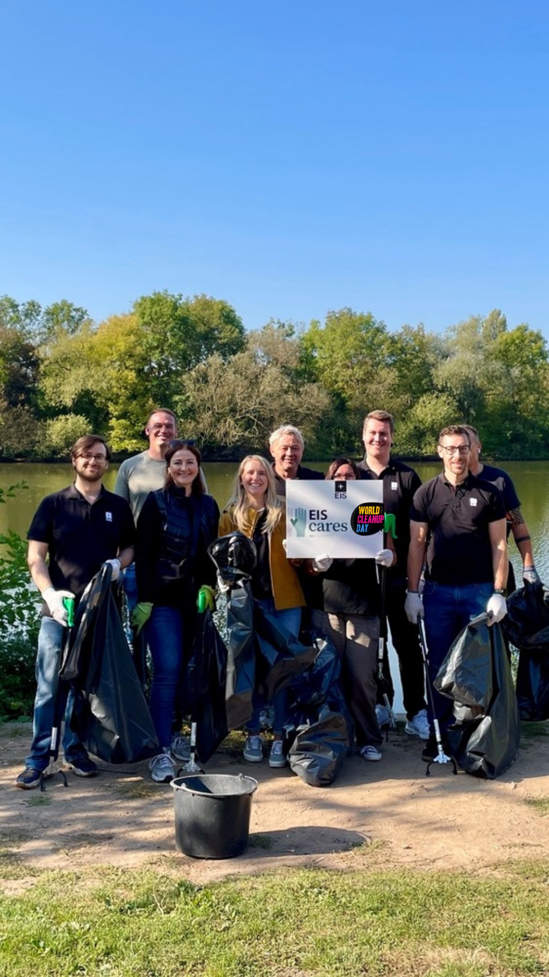 Teamaufstellung des Generalunternehmes aus Aschaffenburg für die Teilnahme World Clean up Day für soziales Engangement. Unsere Projektleiter, Bauleiter, Einkäufer, Buchhalter, Marketing Manager halten volle Müllsäcke in der Hand und stehen vor dem Main, wo sie Müll gesammelt haben für EIS Cares
