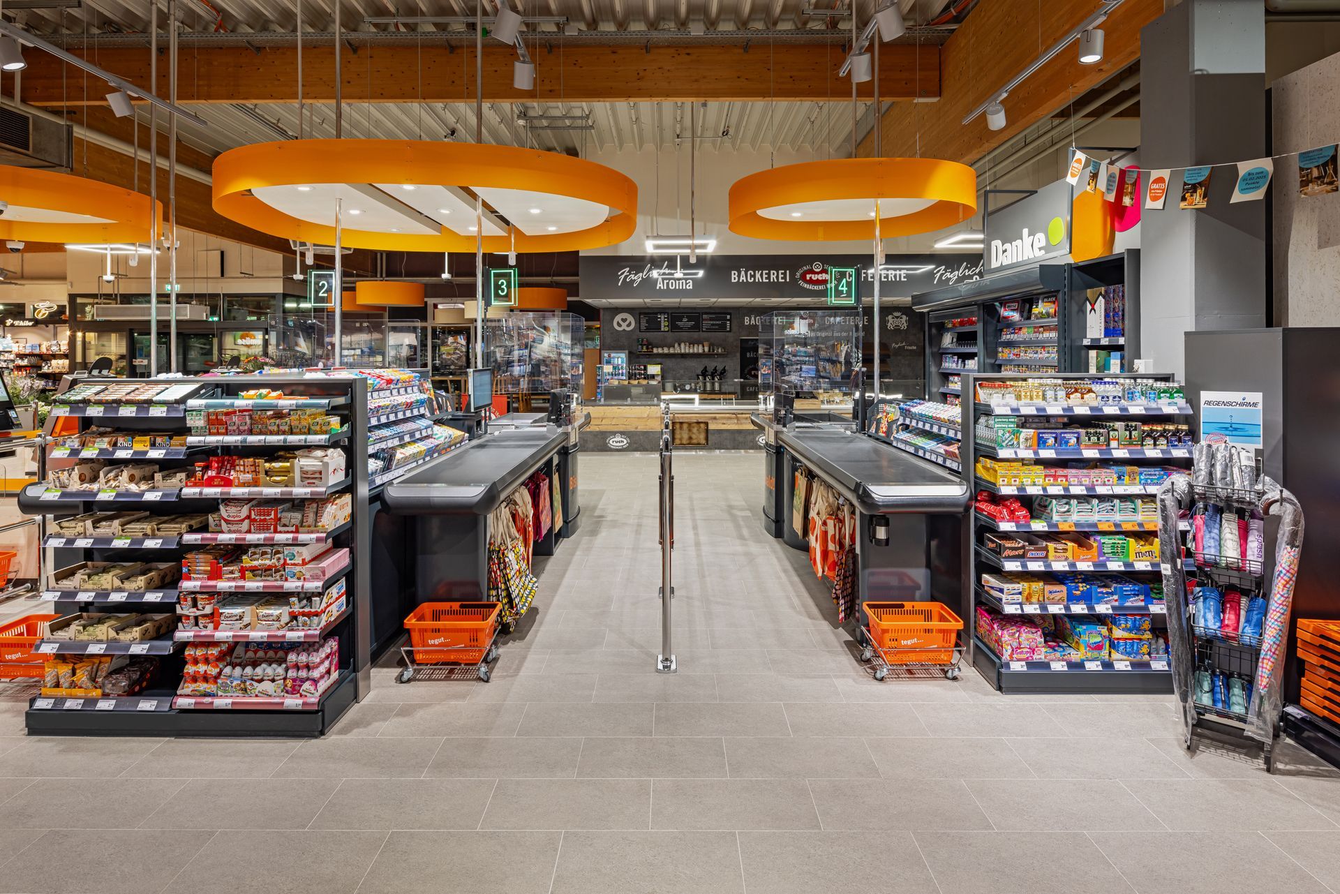 Retail Innenausbau gewerblicher Umbau tegut Supermarkt Witzenhasen - Moderner Kassenbereich in einem Einzelhandelsgeschäft mit auffälliger, oranger Deckenbeleuchtung – Referenzprojekt Ladenbau und Innenausbau Generalunternehmer