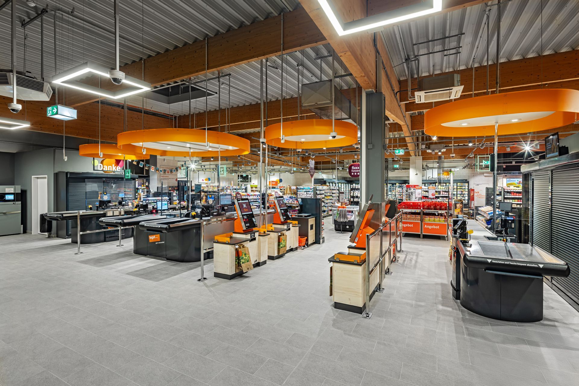 Retail Innenausbau gewerblicher Umbau tegut Supermarkt Witzenhasen - Moderner Kassenbereich in einem Einzelhandelsgeschäft mit auffälliger, oranger Deckenbeleuchtung und effizientem Kassensystem – Referenzprojekt Ladenbau und Innenausbau Generalunternehmer