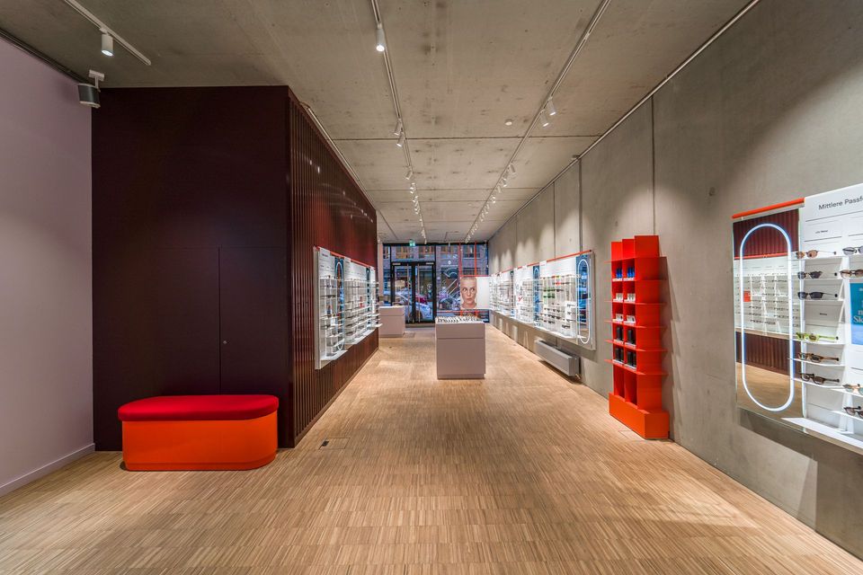 Retail Innenausbau Ladenbau Innenansicht von Ace & Tate Brillengeschäfts in Berlin - Moderner Raum mit roter Wellblechwand und Holzboden - Schlüsselfertiger Innenausbau Generalunternehmung