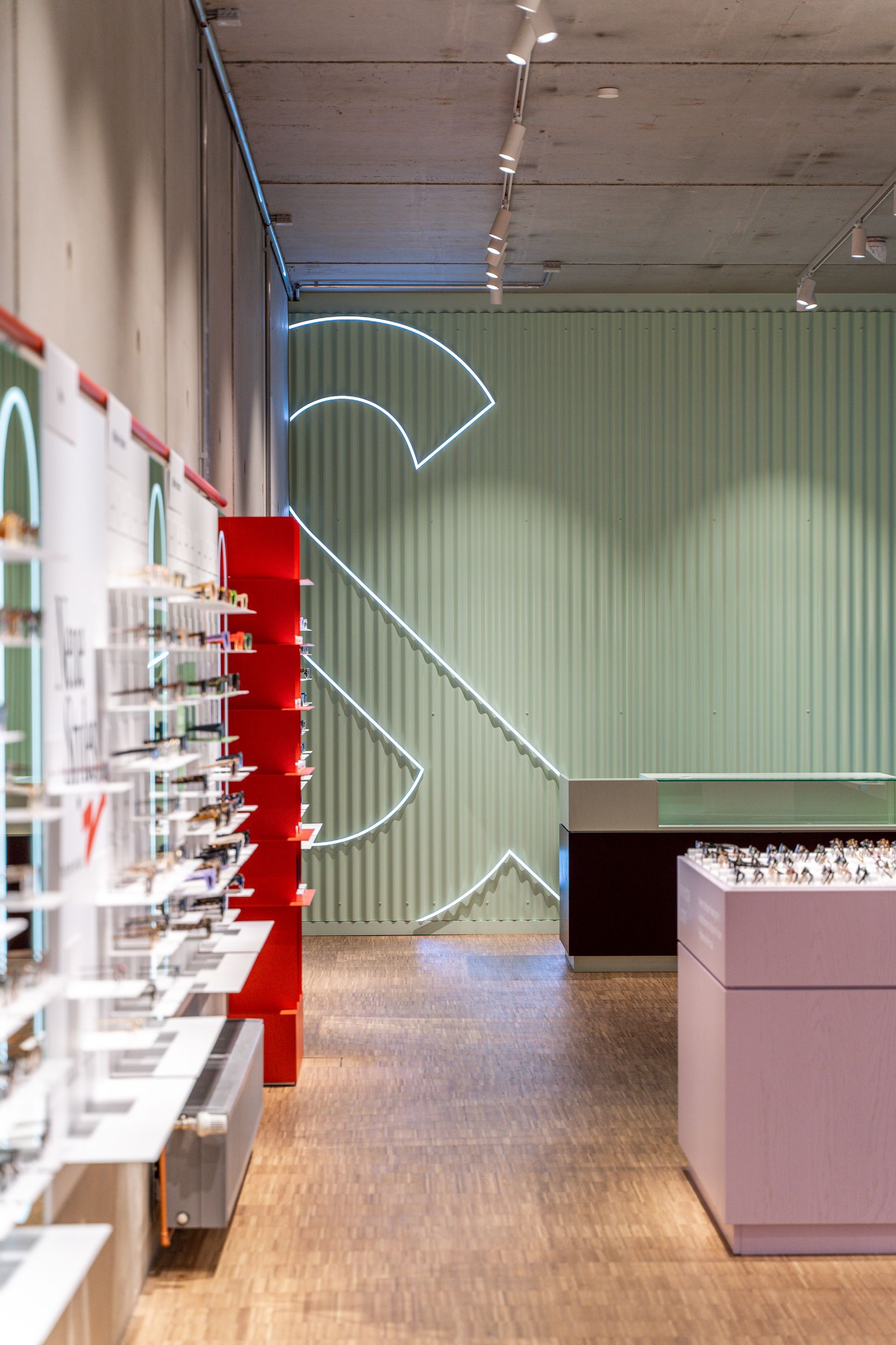 Gewerblicher Innenausbau Retail Einzelhandel ace & tate Brillengeschäft Berlin - Brillenladen mit minzgrünem Wellblech als Wandverkleidung und weißes Neonlicht des Logos - Referenzprojekt Ladenbau und Innenausbau Generalunternehmer