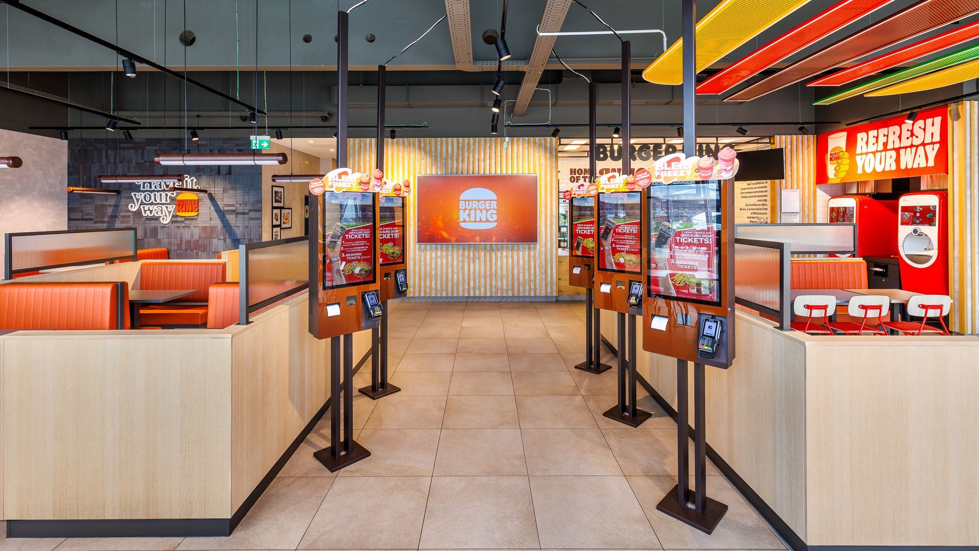 Restaurantumbau Burger King Vösendorf - Eingangbereich mit digitalen Bestellschaltern und Holzwandverkleidung, modernen Tischen und Stühlen - Referenzprojekt Ladenbau und Innenausbau Generalunternehmer