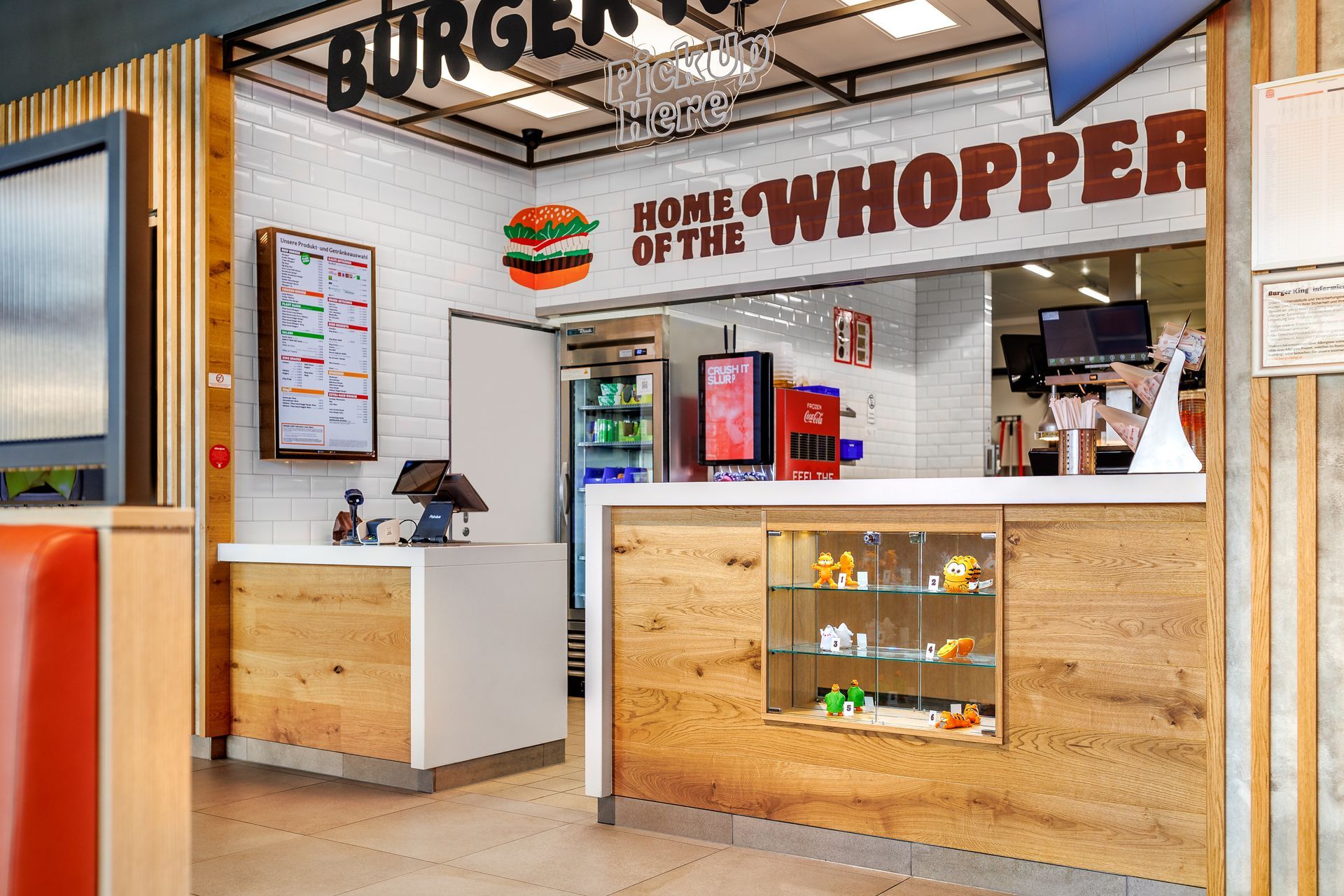 Restaurantumbau Burger King Vösendorf - Tresenbereich im Gastronomie-Ladenbau mit Kassen- und Abholtheke, natürlicher Holzverkleidung, digitalem Menü-Display und Wanddekoration – Referenzprojekt Ladenbau und Innenausbau Generalunternehmer
