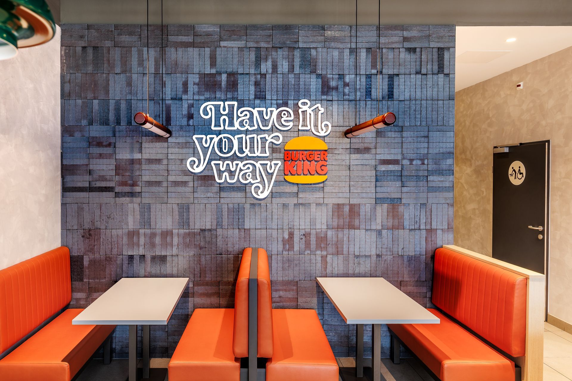 Restaurantumbau Burger King Vösendorf - Kreative Wandgestaltung im Gastronomie-Interieur mit urbaner Backstein-Optik, Neon-Leuchtschrift ‚Have it your way‘ und Polstersitzbänken – Referenzprojekt Ladenbau und Innenausbau Generalunternehmer