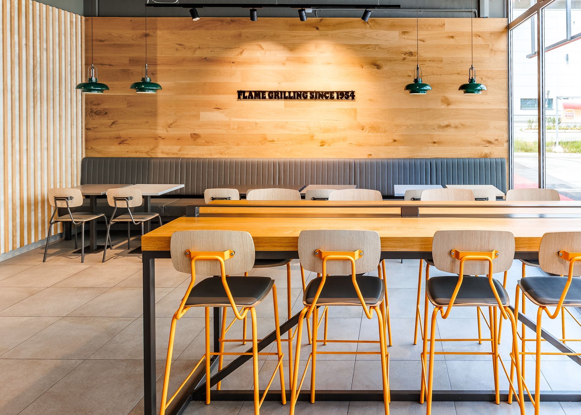 Restaurantumbau Burger King Vösendorf - Langer Sitzbereich im Gastronomie-Interieur mit grauer Polsterbank, Holzwandverkleidung und modernen Tischen und Stühlen. Wanddekor mit 