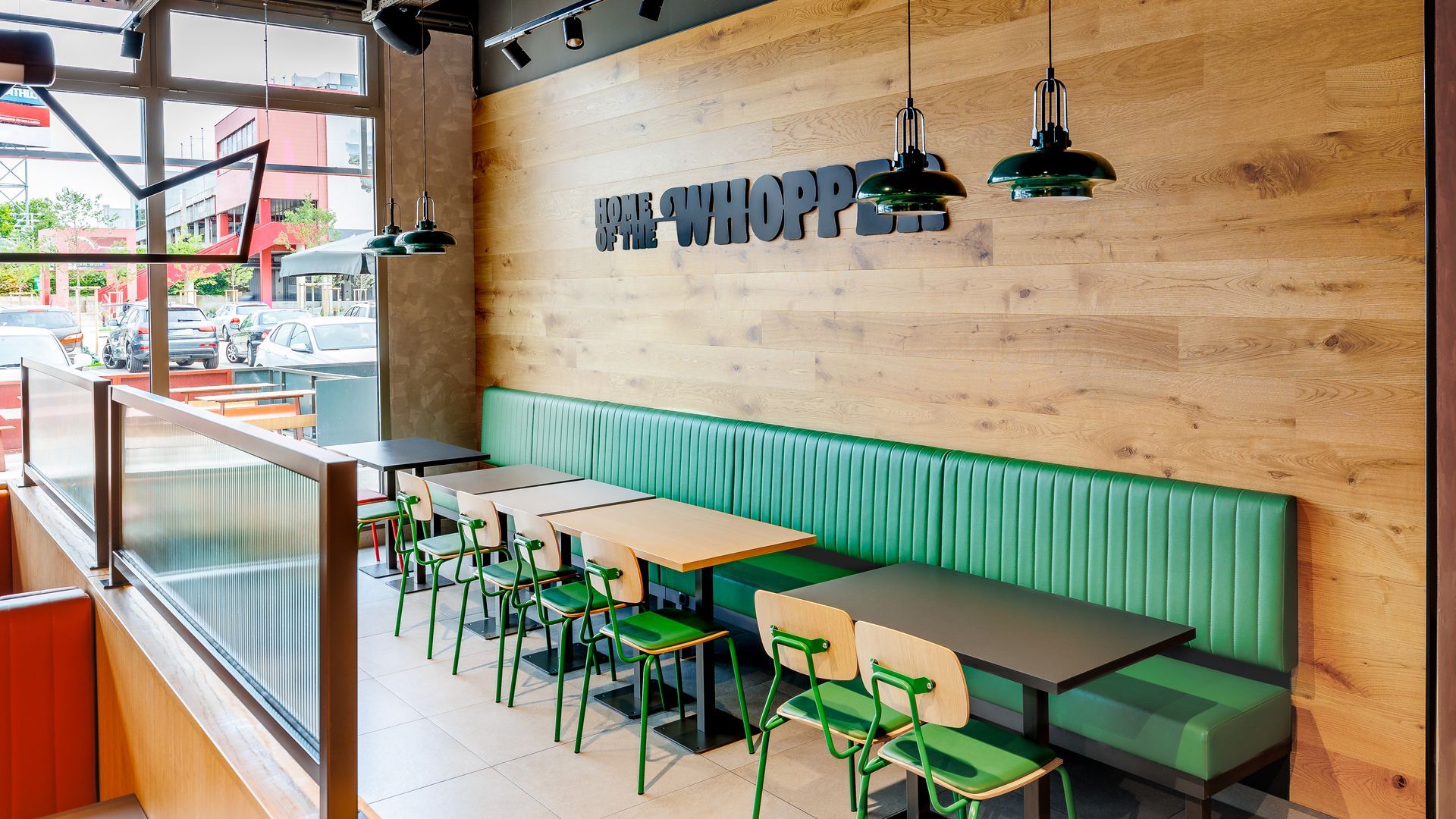 Restaurantumbau Burger King Vösendorf - Langer Sitzbereich im Gastronomie-Interieur mit grüner Polsterbank, Holzwandverkleidung und modernen Tischen und Stühlen. Wanddekor mit 