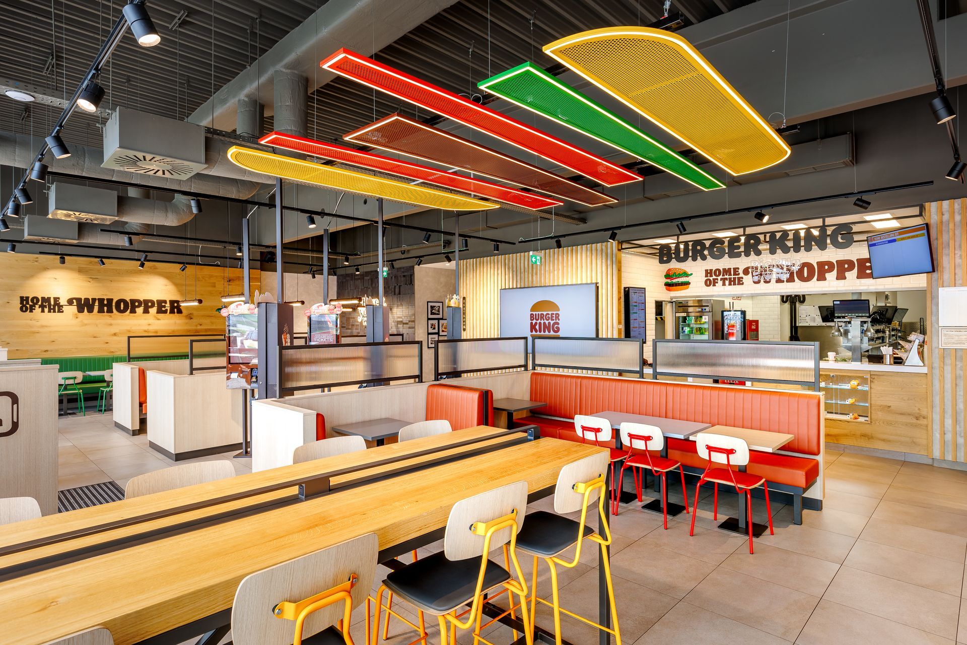 Restaurantumbau Burger King Vösendorf - Modernes Gastronomie-Interieur mit warmen Holzelementen, vielseitigen Sitzbereichen und auffälliger, farbiger Deckenbeleuchtung in Burgerform – Referenzprojekt Ladenbau und Innenausbau Generalunternehmer