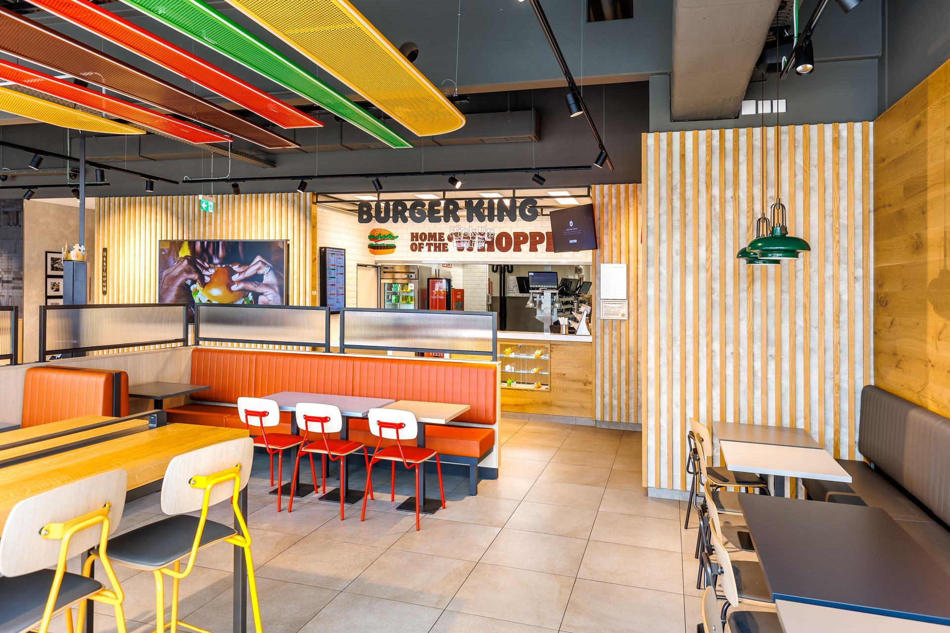 Restaurantumbau Burger King Vösendorf - Modernes Gastronomie-Interieur mit warmen Holzelementen, Sitzbereichen und bunter Deckenbeleuchtung in Burgerform – Referenzprojekt Ladenbau und Innenausbau Generalunternehmer