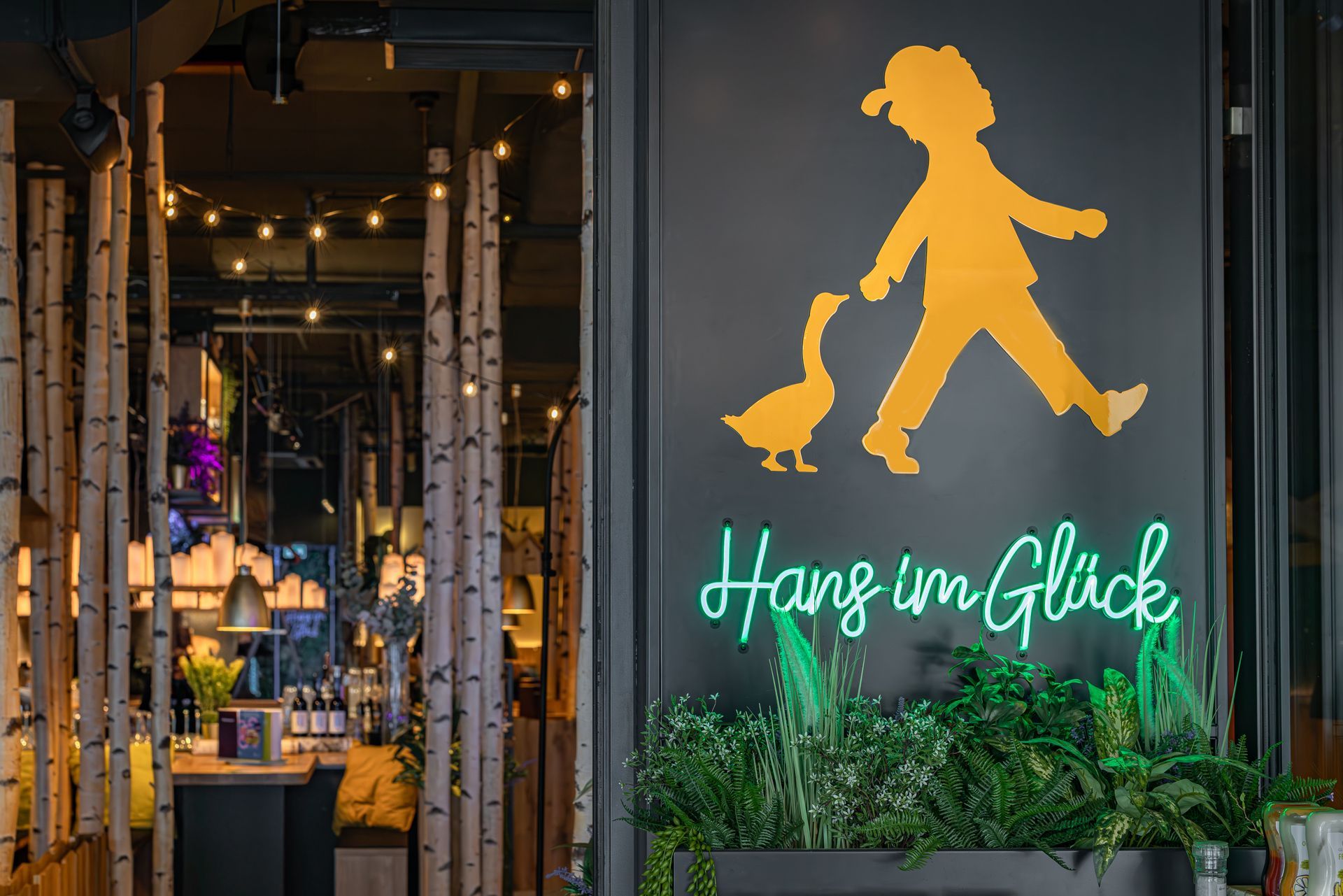 Hans im Glück Berlin - Moderner Gastronomie-Eingangsbereich mit dekorativem Logo, Pflanzen und stimmungsvollem Innenausbau - Referenzprojekt Restaurantumbau Generalunternehmer Innenausbau