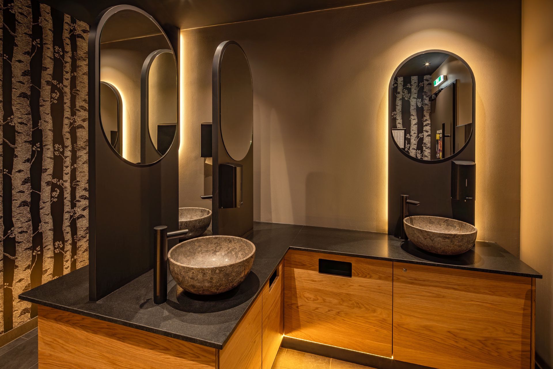 Hans im Glück Wien - Restaurant Badezimmer, Toilettenbereich mit dekorativen Spülbecken aus Stein, beleuchteten Spiegeln und stilvoller Inneneinrichtung – Referenzprojekt Restaurantumbau Generalunternehmer Innenausbau