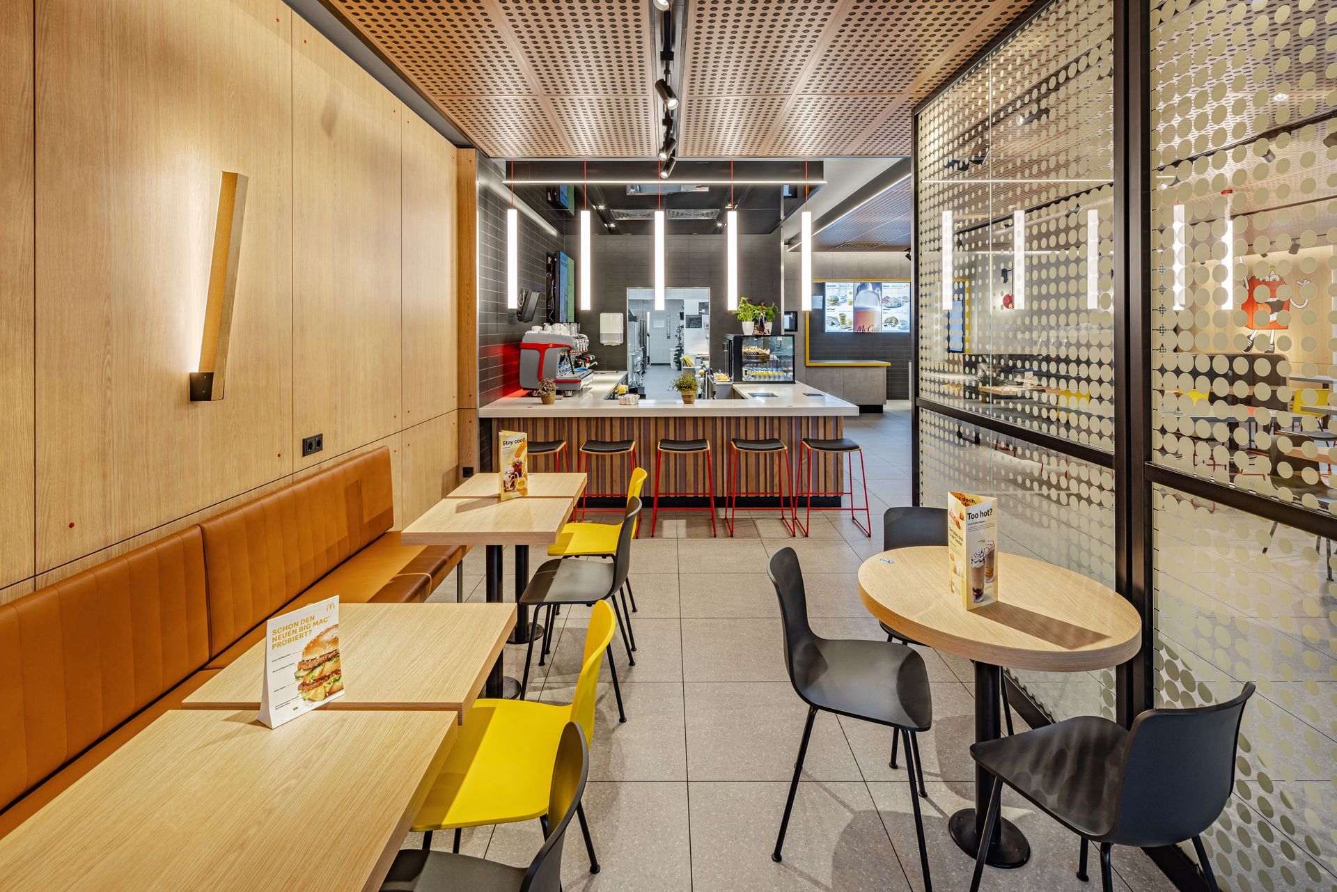McDonald's Ray Bochum - Restaurantumbau - Schreinermöbel aus Holz,Ledersitzbänke und Eichen Holztische, Glastrennwand und Bick auf das McCafé - Referenzprojekt Generalunternehmer Innenausbau