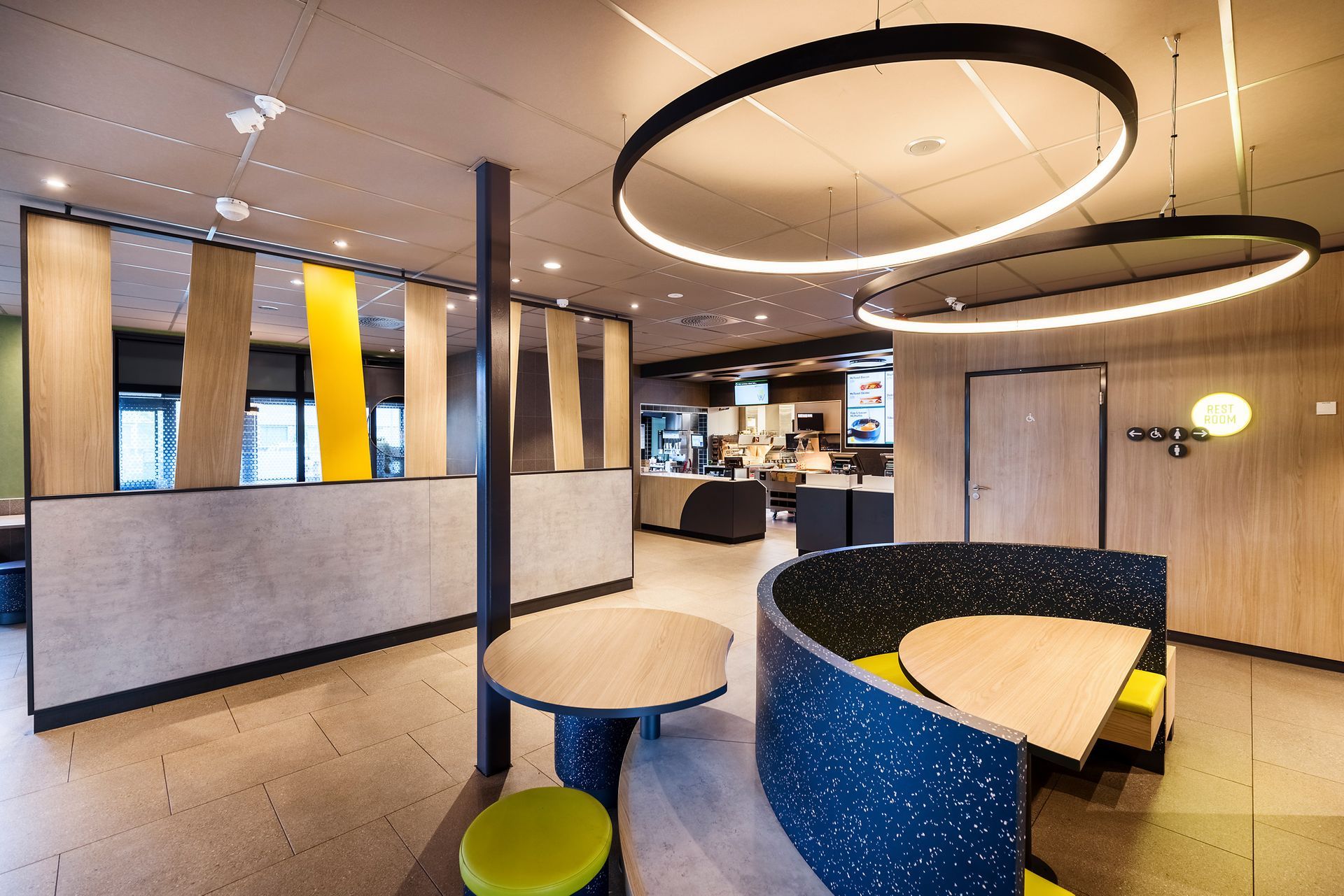 McDonald's Luna Gardermoen - modernen Fast-Food-Restaurant, mit runder, hochlehniger Sitzbank und einem integrierten Holztisch, hellgelben Hocker - Referenzprojekt Generalunternehmer Innenausbau
