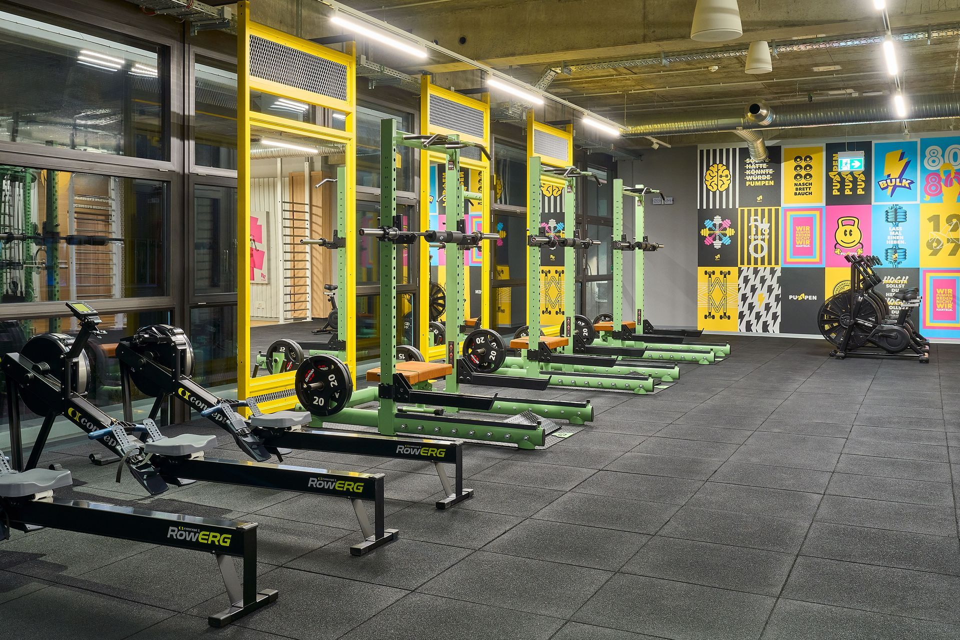 Innenausbau Fitnessstudio McFIT München Forstenried - Funktioneller Trainingsbereich im Fitnessstudio mit Rudergeräten, Hantelracks, moderner Beleuchtung und farbigen Wandgrafiken - Referenzprojekt Fitnessstudio Innenausbau Generalunternehmer