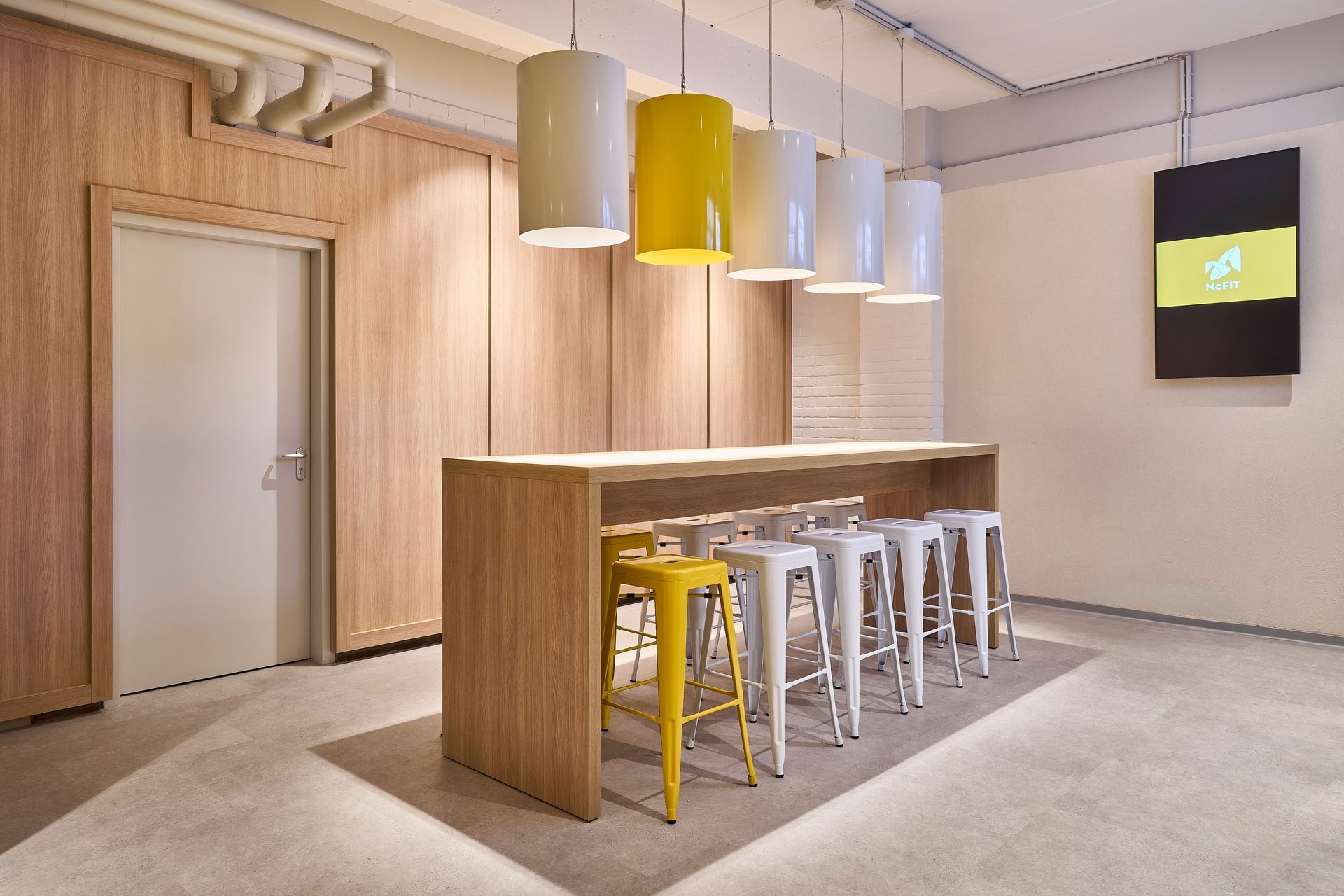 Innenausbau Fitnessstudio McFIT München Schwabing - Eingangsbereich moderne Lounge im Innenausbau mit hoher Bartheke, gelben Hockern, stylischen Deckenlampen - Referenzprojekt Fitnessstudio Innenausbau Generalunternehmer