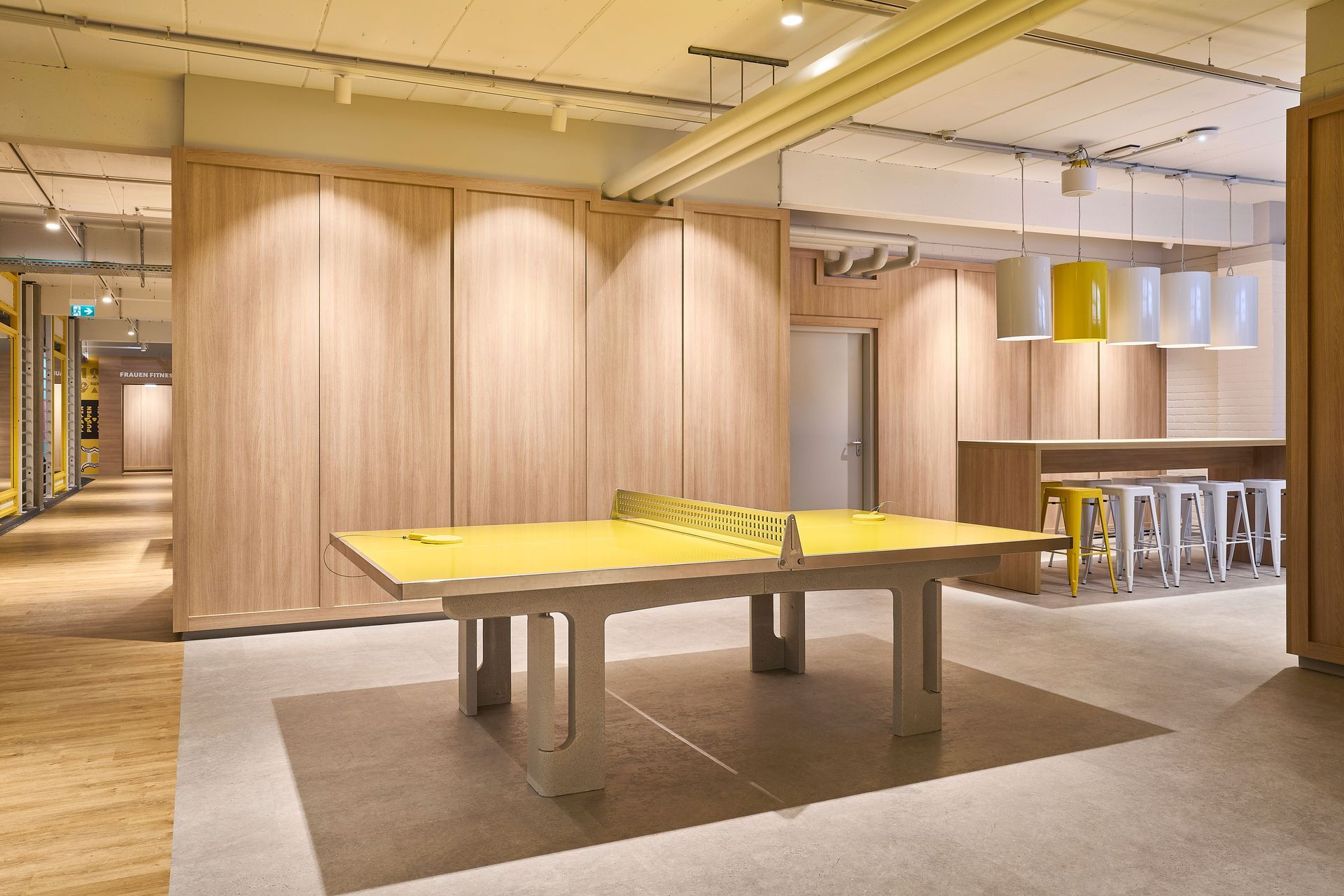 Innenausbau Fitnessstudio McFIT München Schwabing - gelbe Tischtennisplatte, Innenraum mit Holzwandverkleidung - Referenzprojekt Fitnessstudio Innenausbau Generalunternehmer