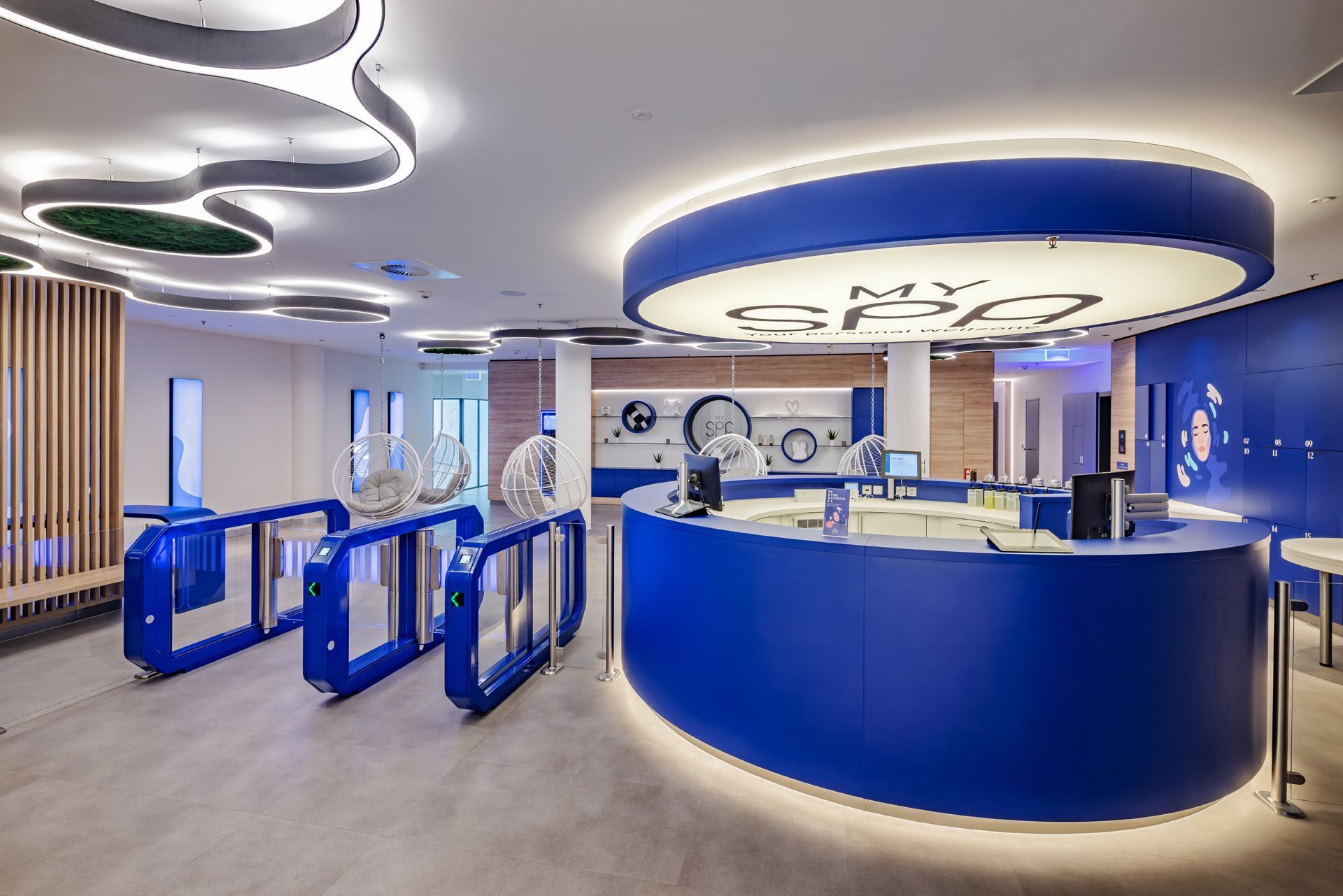 Wellness und Spa Einrichtung MySpa Mannheim Innenausbau - Moderner und futuristischer Empfangsbereich mit geschwungenem blauen Tresen, digitaler Beschilderung und weißen Deckenleuchten in Form von Kreisen - Referenzprojekt im Bereich Spa und Wellness Generalunternehmer
