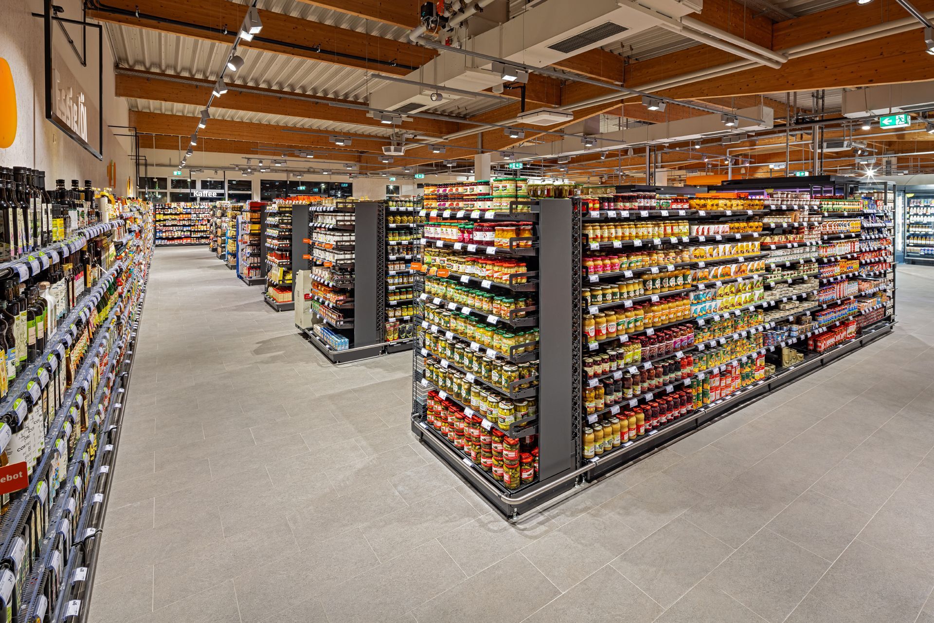 Innenausbau-Projekt Einzelhandel Ladenbau tegut, Witzenhausen - Geräumiger Supermarkt mit Produktregalen, heller Beleuchtung. Orange Akzente dominieren - Referenzprojekt Retail Innenausbau Generalunternehmer