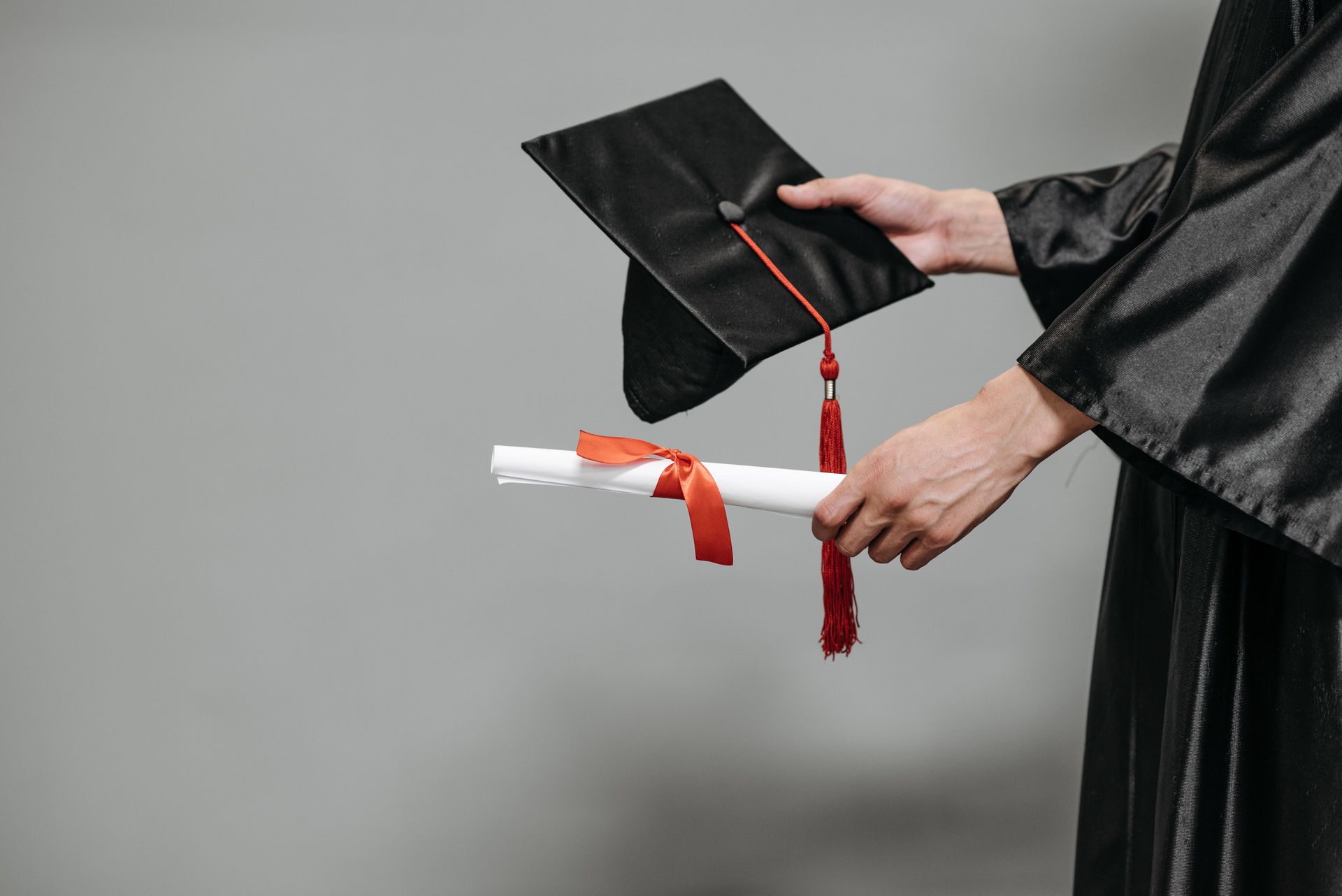 Mani che reggono un diploma e un cappello da laurea nero con nappa rossa.