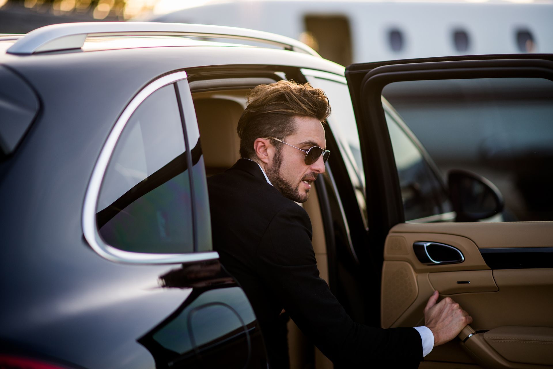 Man in sunglasses stepping out of a black luxury car with a beige interior