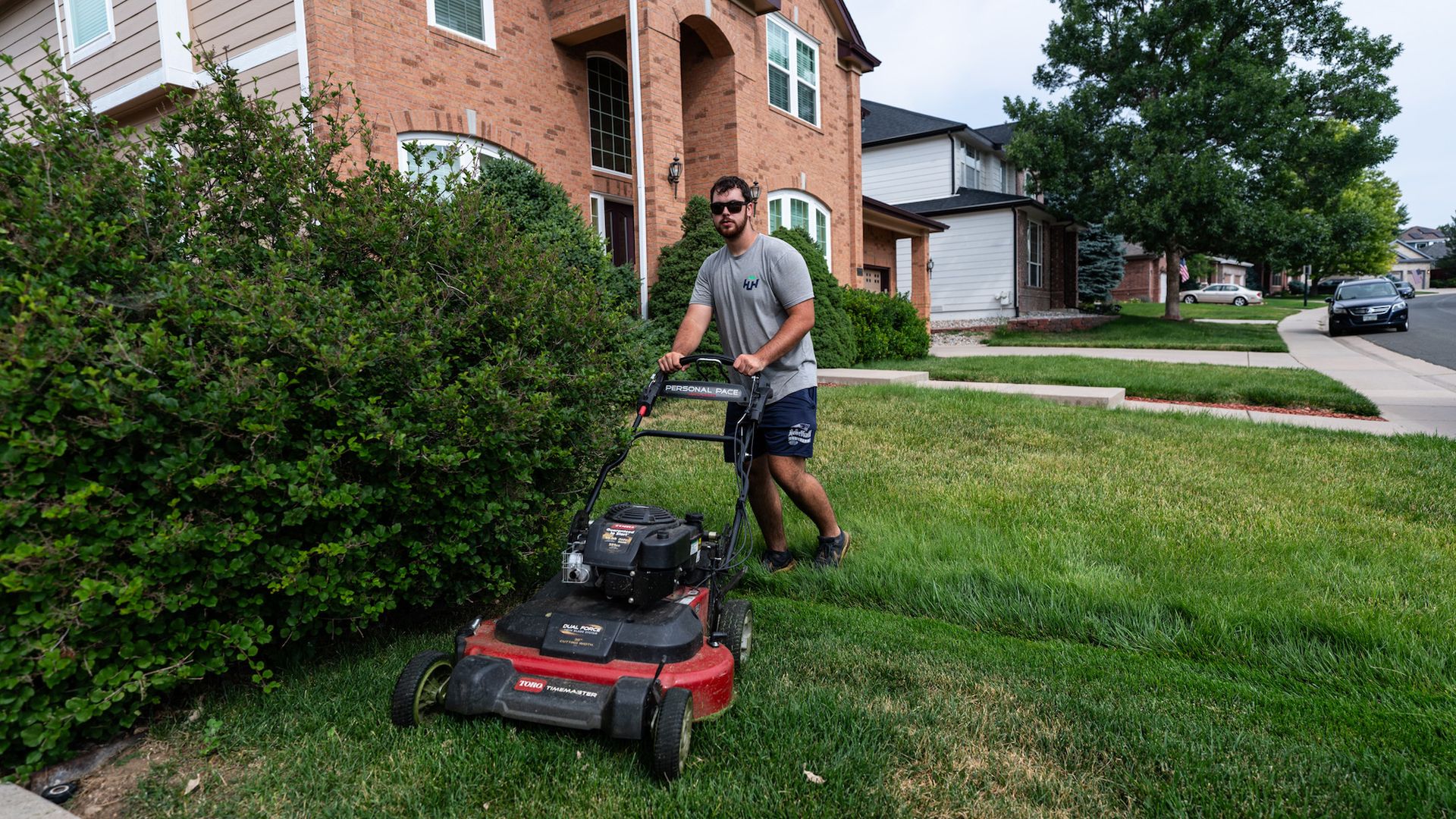 A man is using a lawn mower to cut the grass in front of a house.