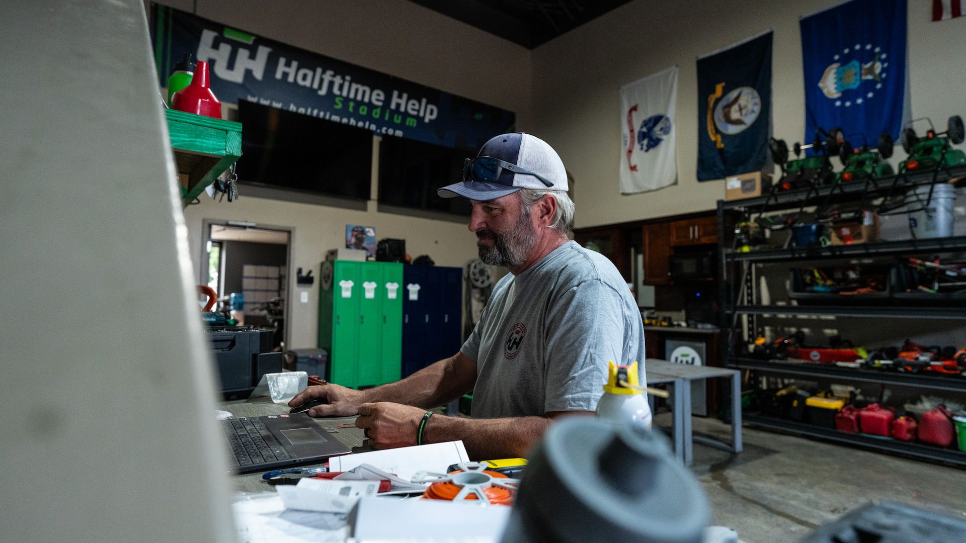 A man is sitting at a desk in a garage using a laptop computer.