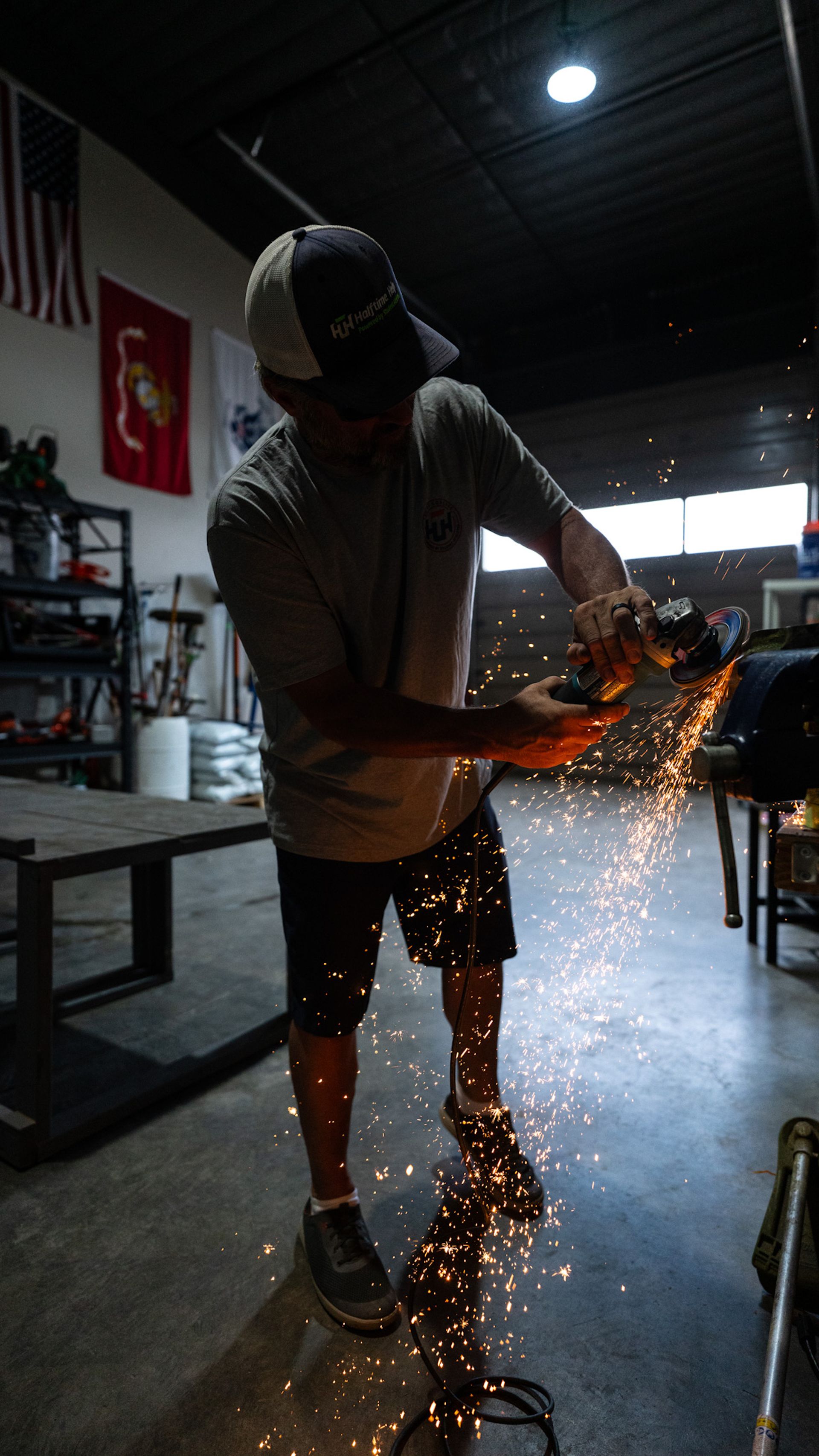 A man is cutting a piece of metal with a grinder in a workshop.