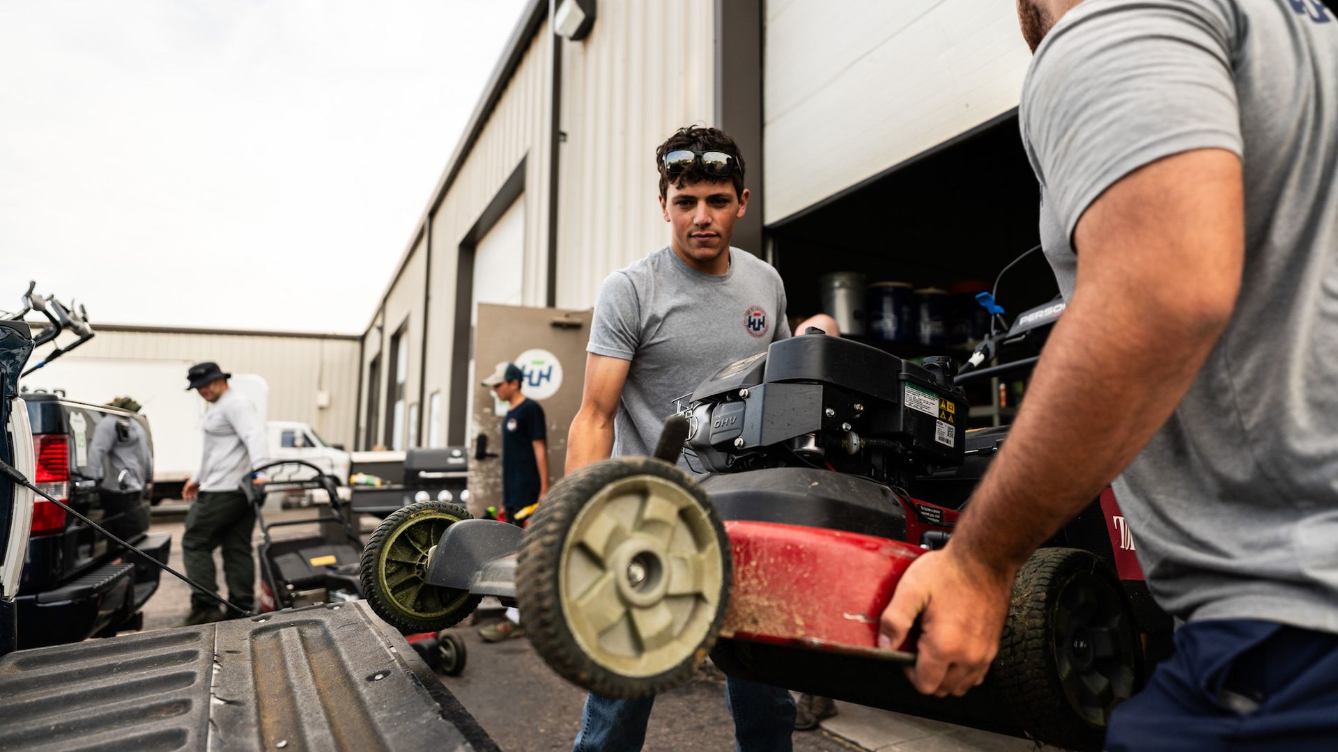 Two men are carrying a lawn mower into a garage.