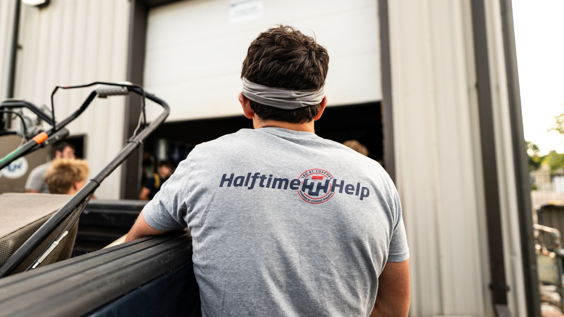 A man wearing a halftime help t-shirt is sitting in the back of a truck.