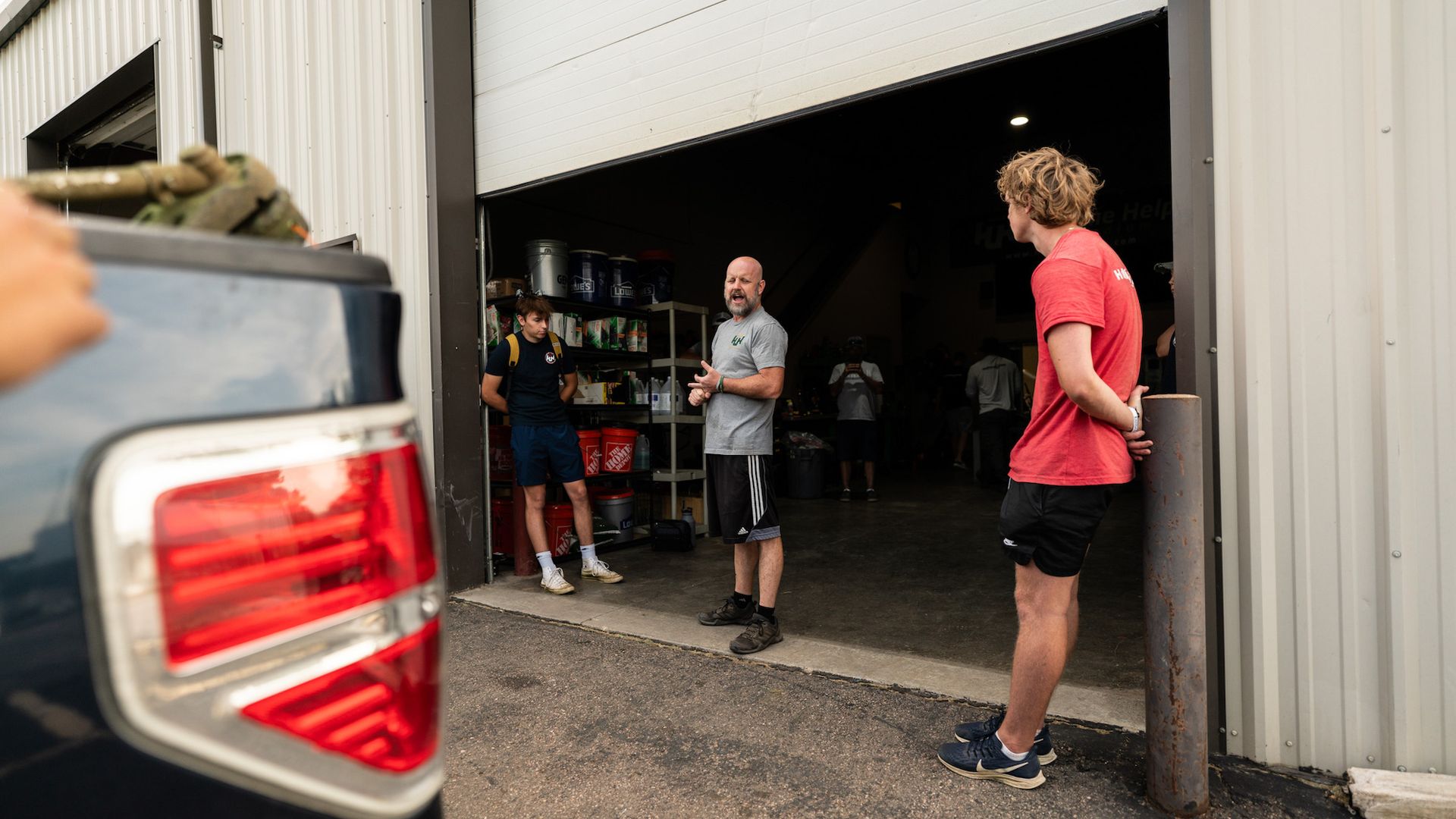 A group of men are standing outside of a garage talking to each other.
