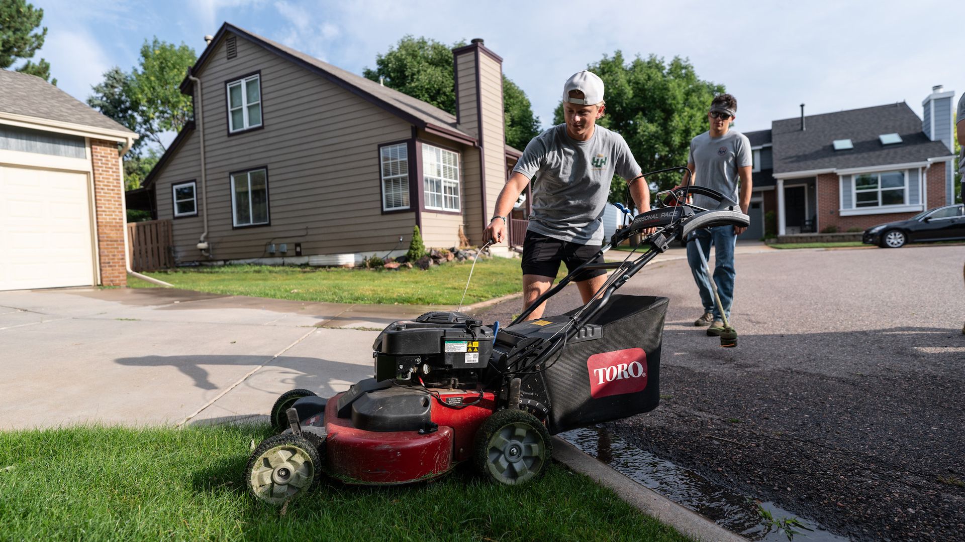 A man is using a lawn mower to cut the grass in front of a house.