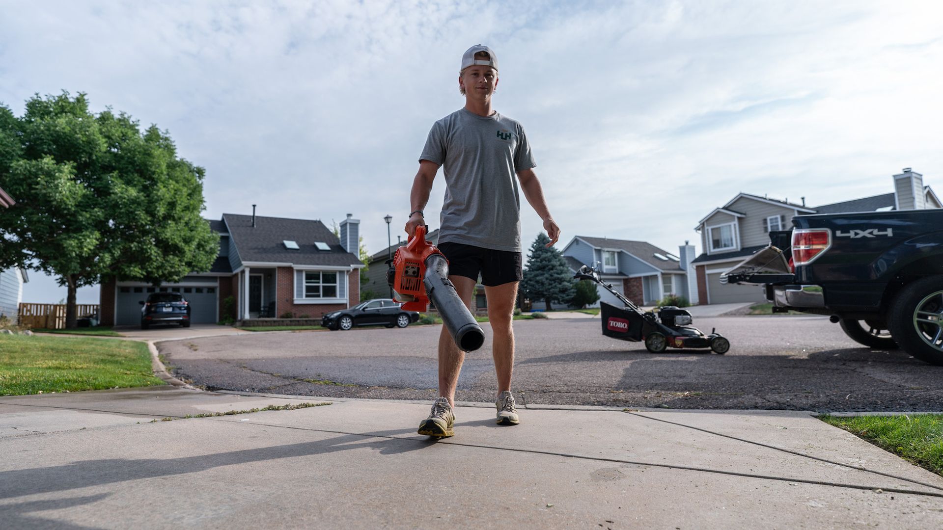 A man is walking down a sidewalk with a blower in his hand.