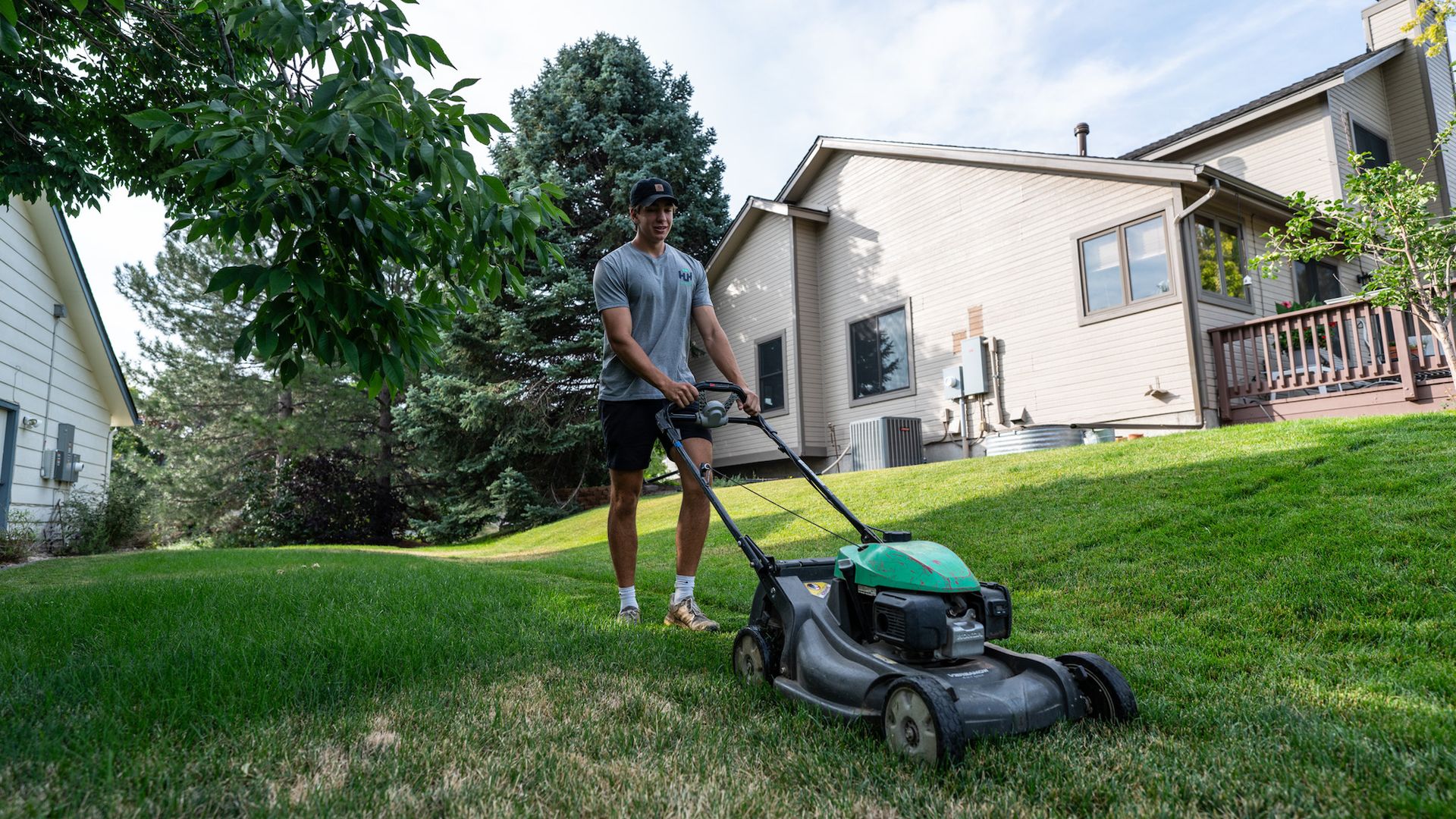 A man is using a lawn mower to cut the grass in front of a house.