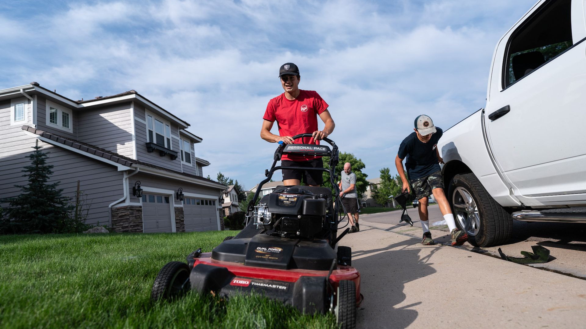 A man is using a lawn mower to cut the grass in front of a house.