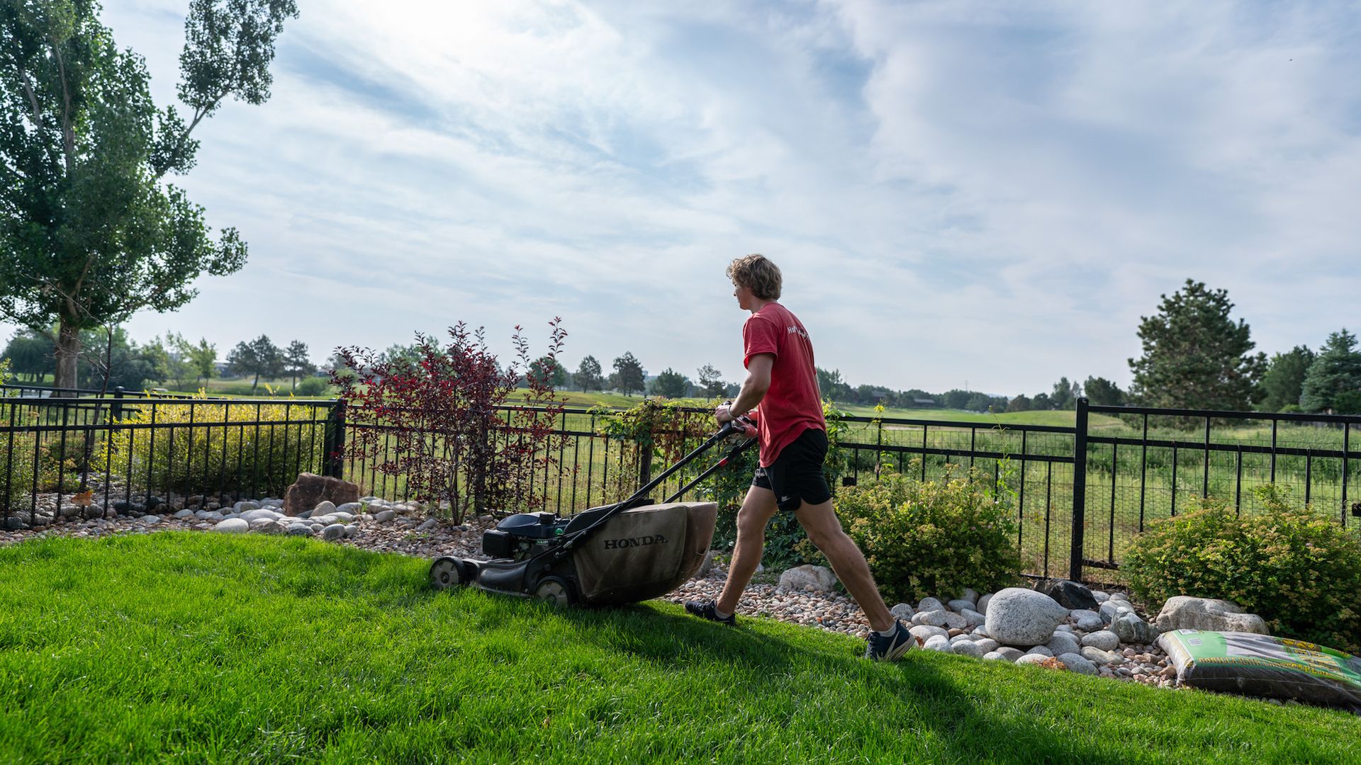 A man on a ed shirt using a lawn mower.