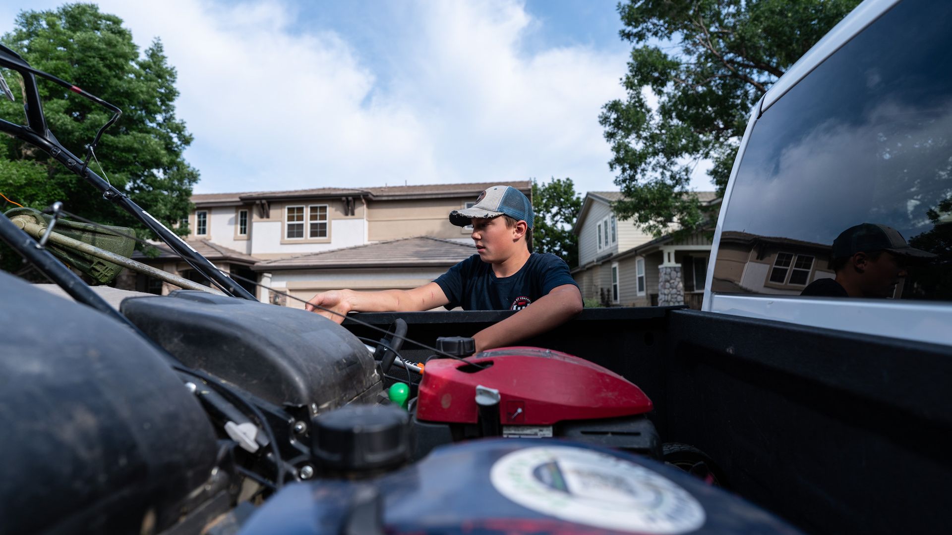 A man is working on a lawn mower in the back of a truck.