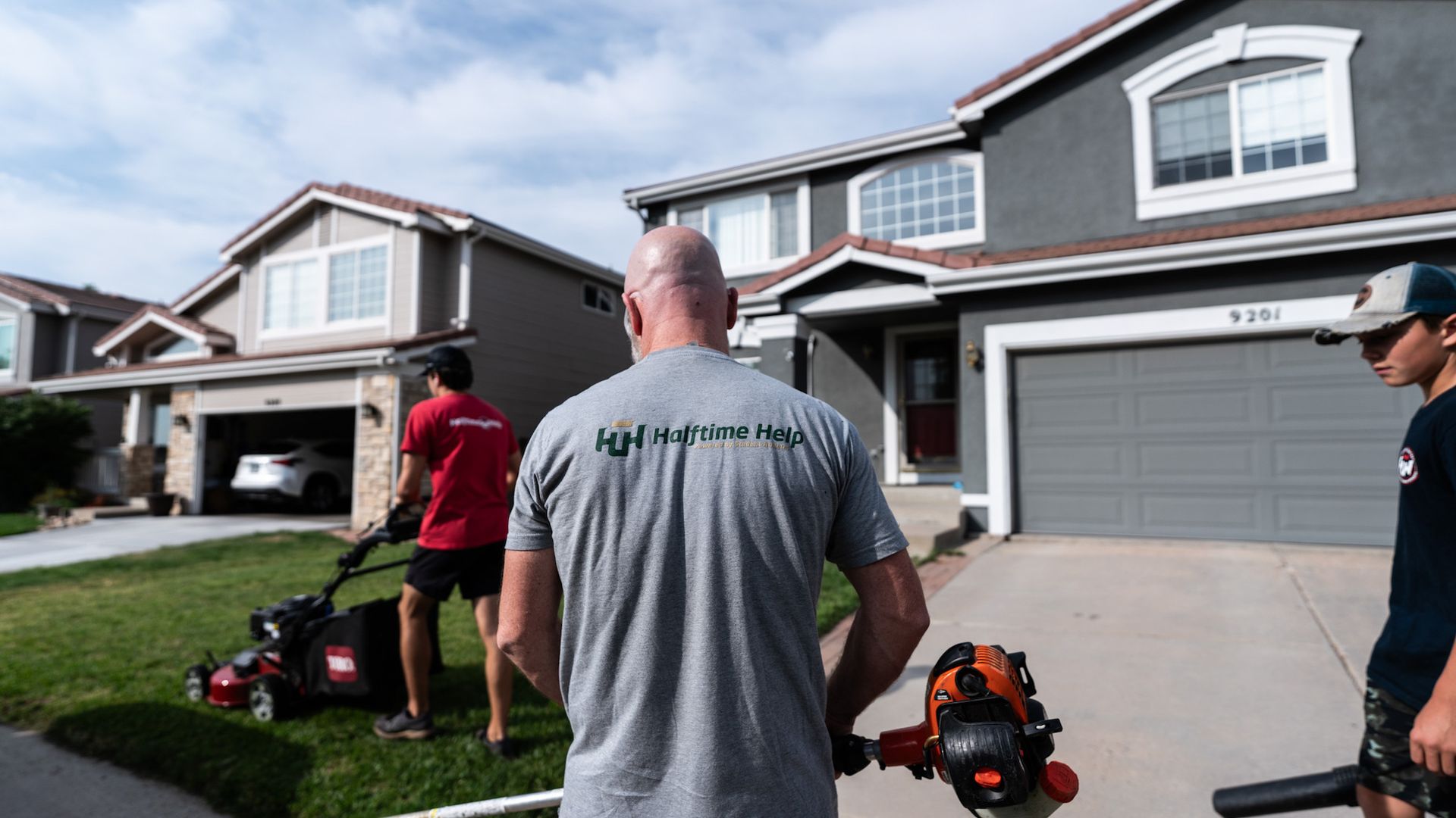 A man is standing in front of a house holding a lawn mower.