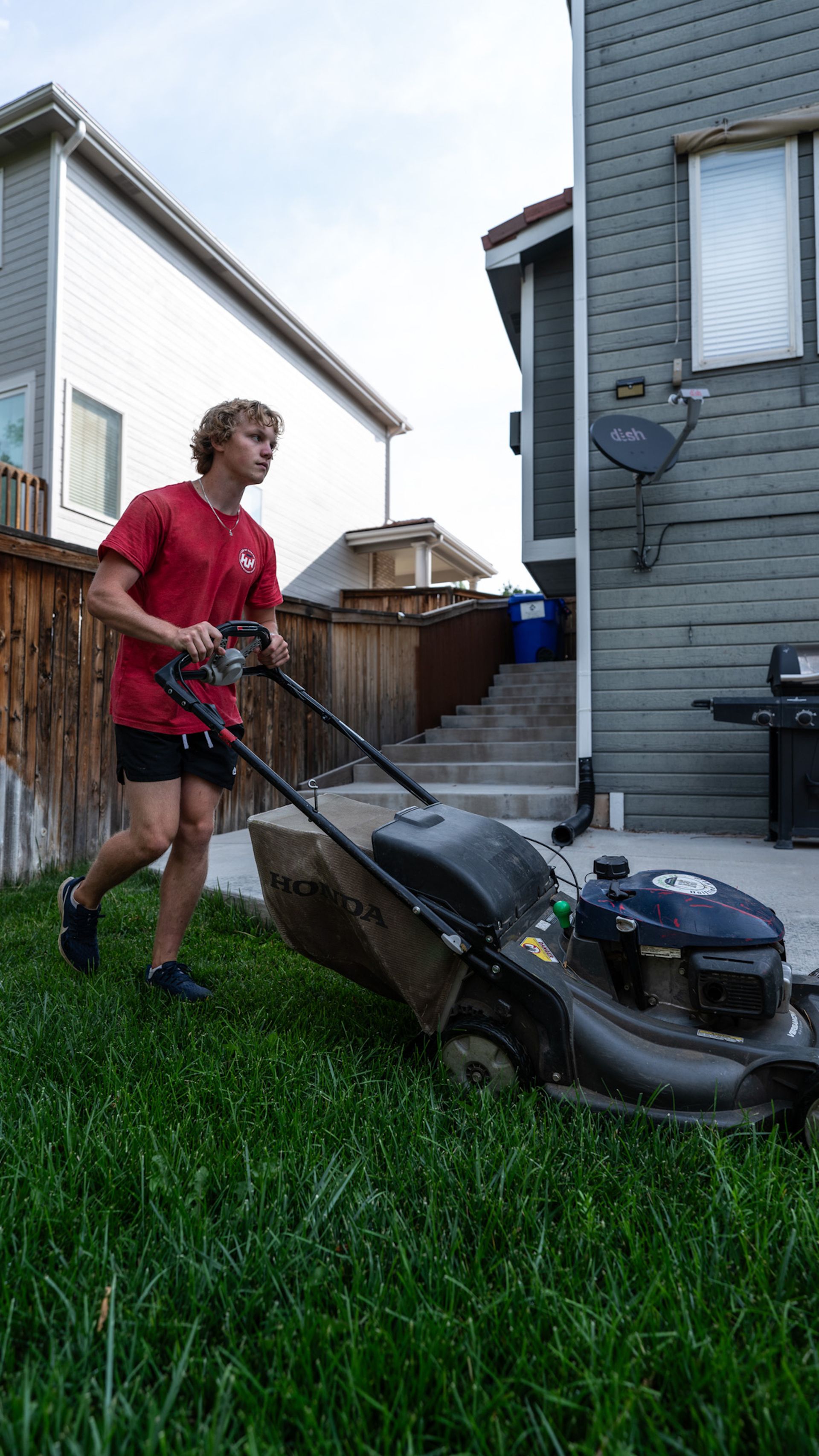 A young man is mowing his lawn with a lawn mower.