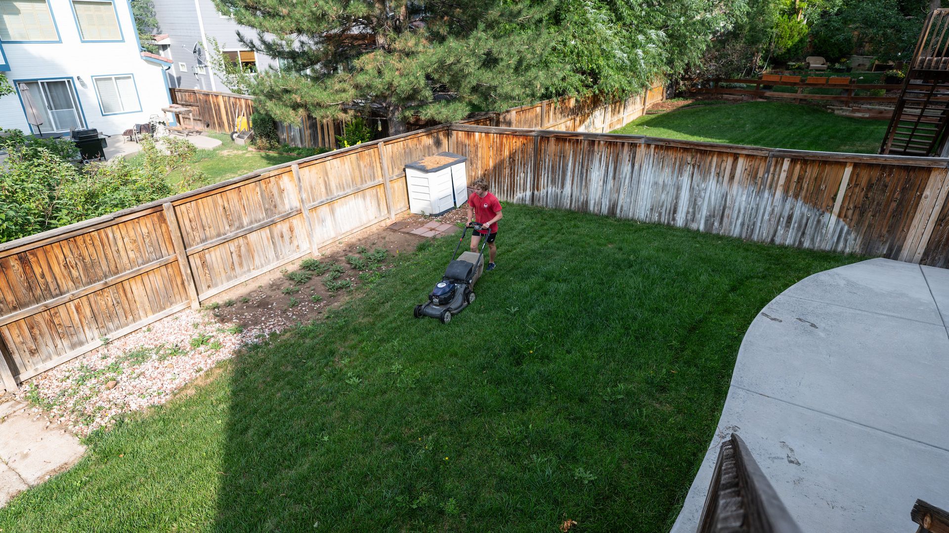 A man is using a lawn mower to cut the grass in a backyard.