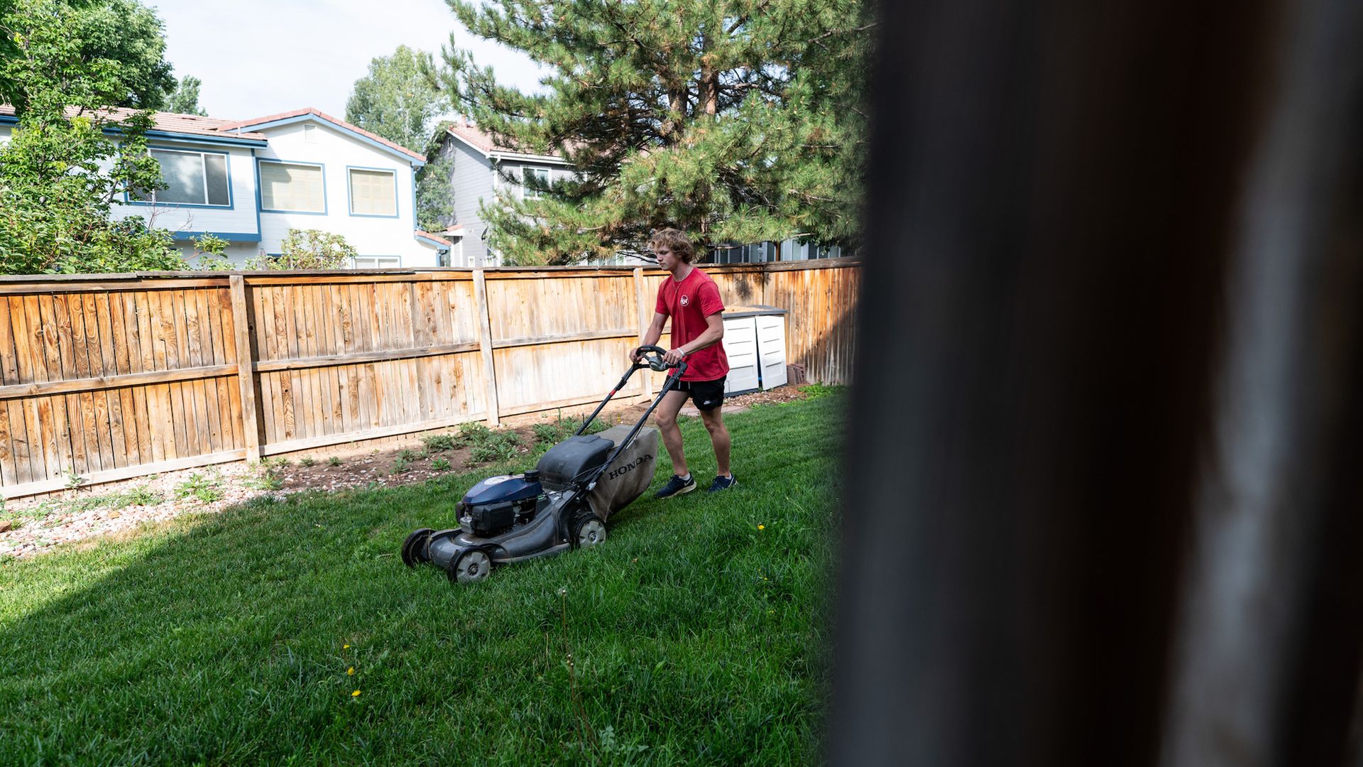 A man is using a lawn mower to cut the grass in his backyard.