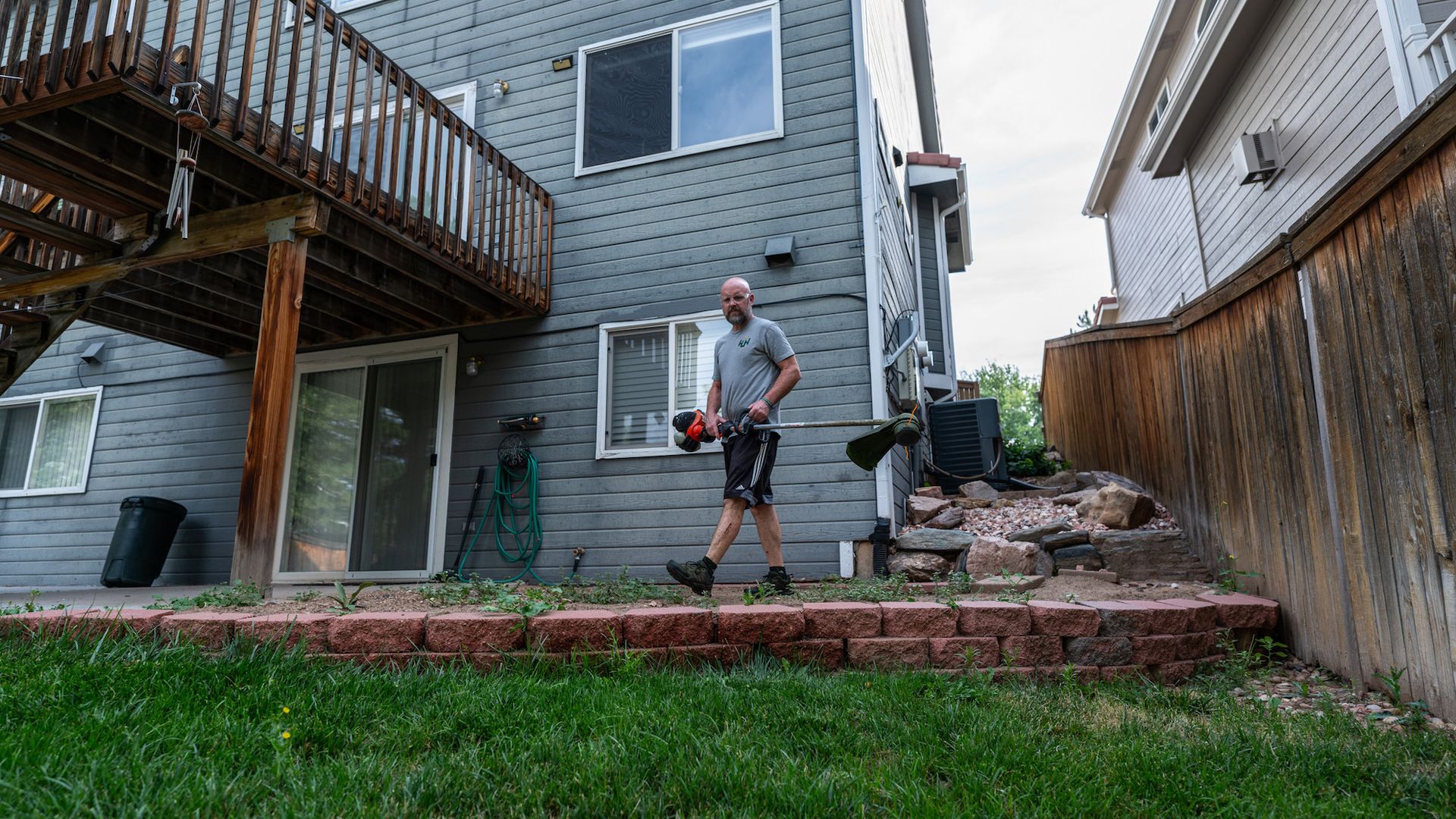 A man is standing in the backyard of a house holding a chainsaw.