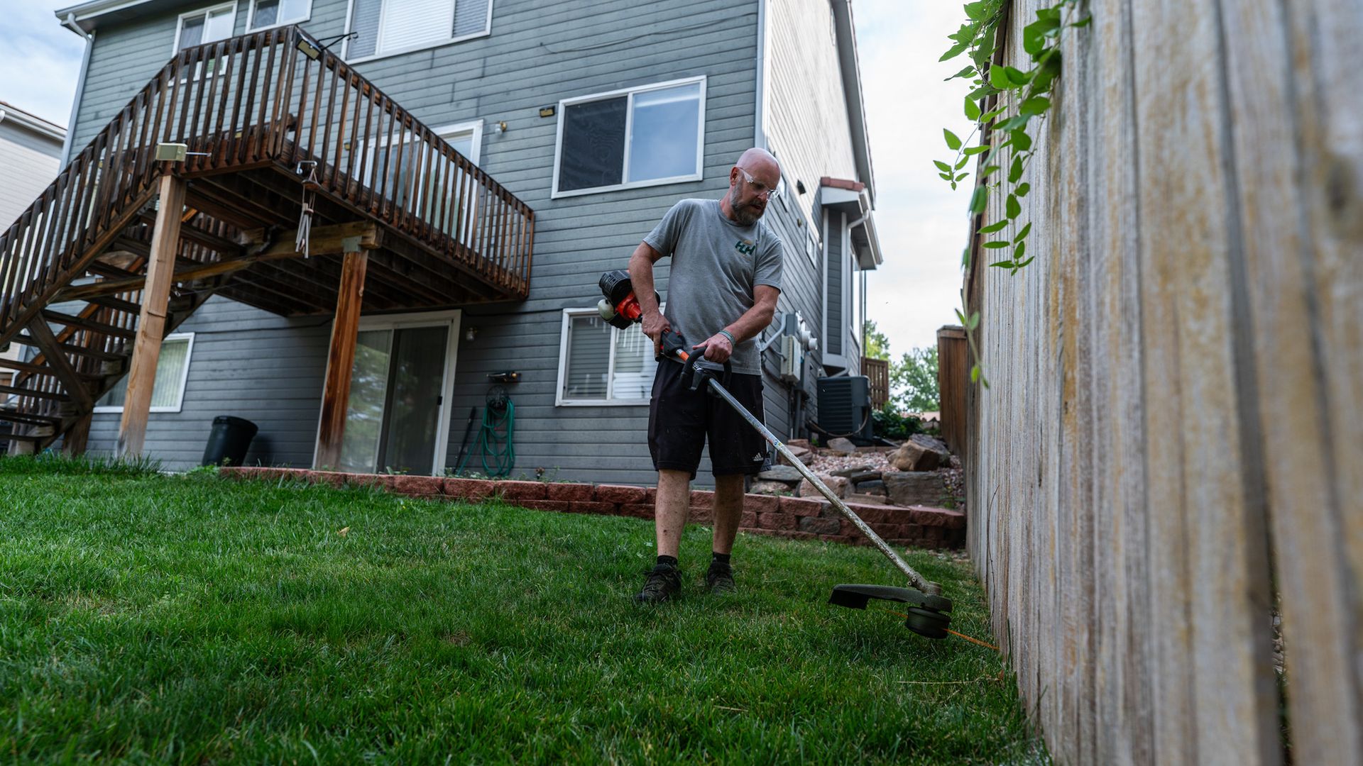 A man is using a lawn mower to cut the grass in his backyard.