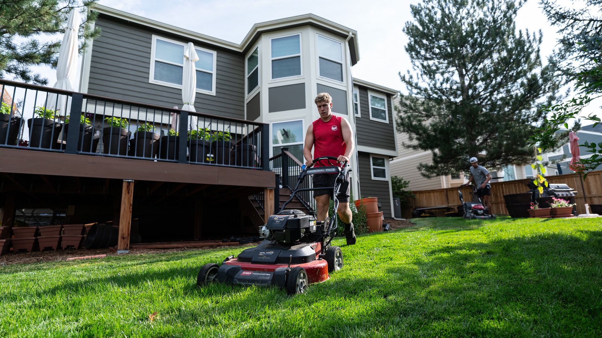 A man is mowing a lush green lawn in front of a house.