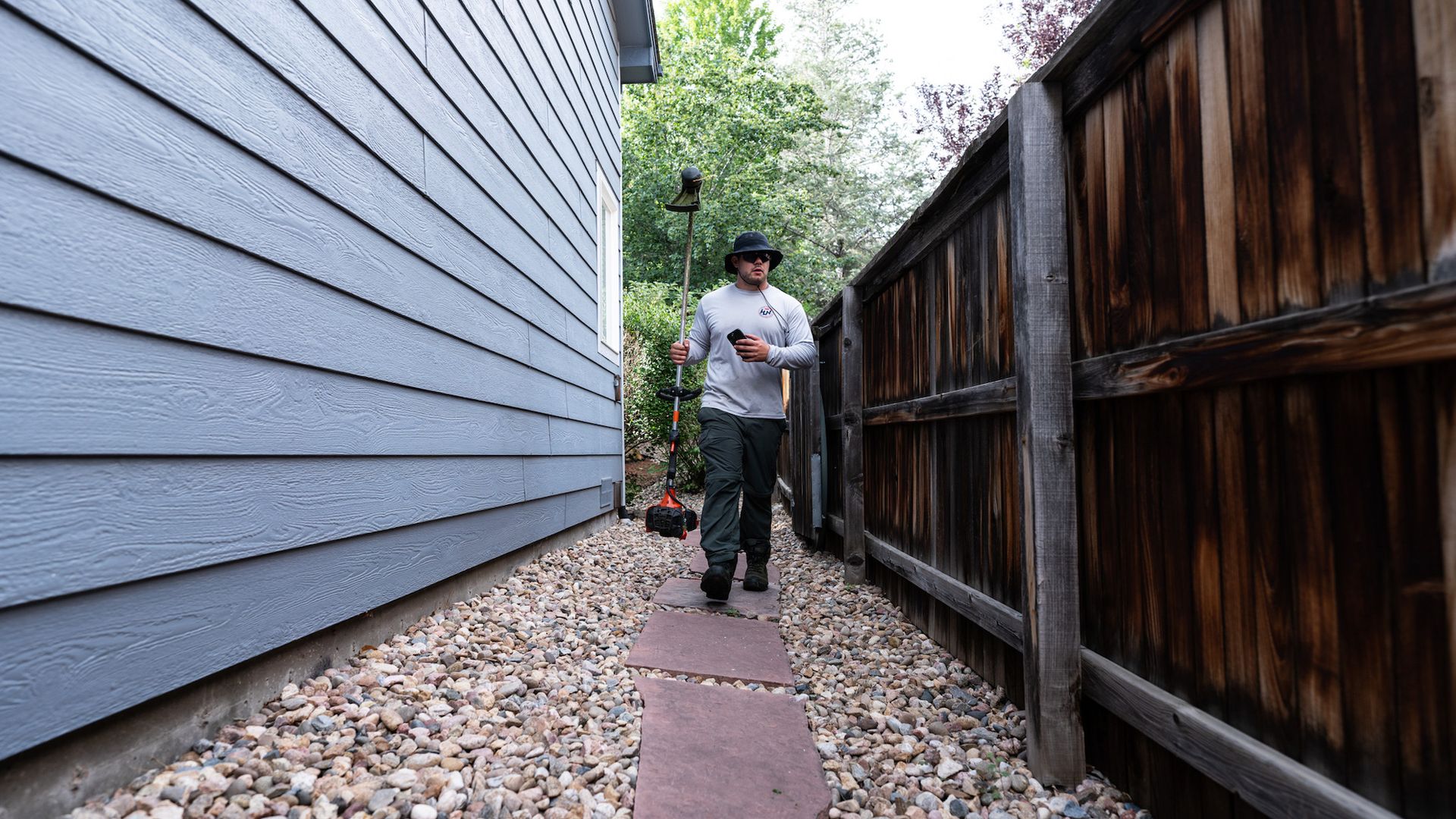 A man is walking down a sidewalk next to a wooden fence.