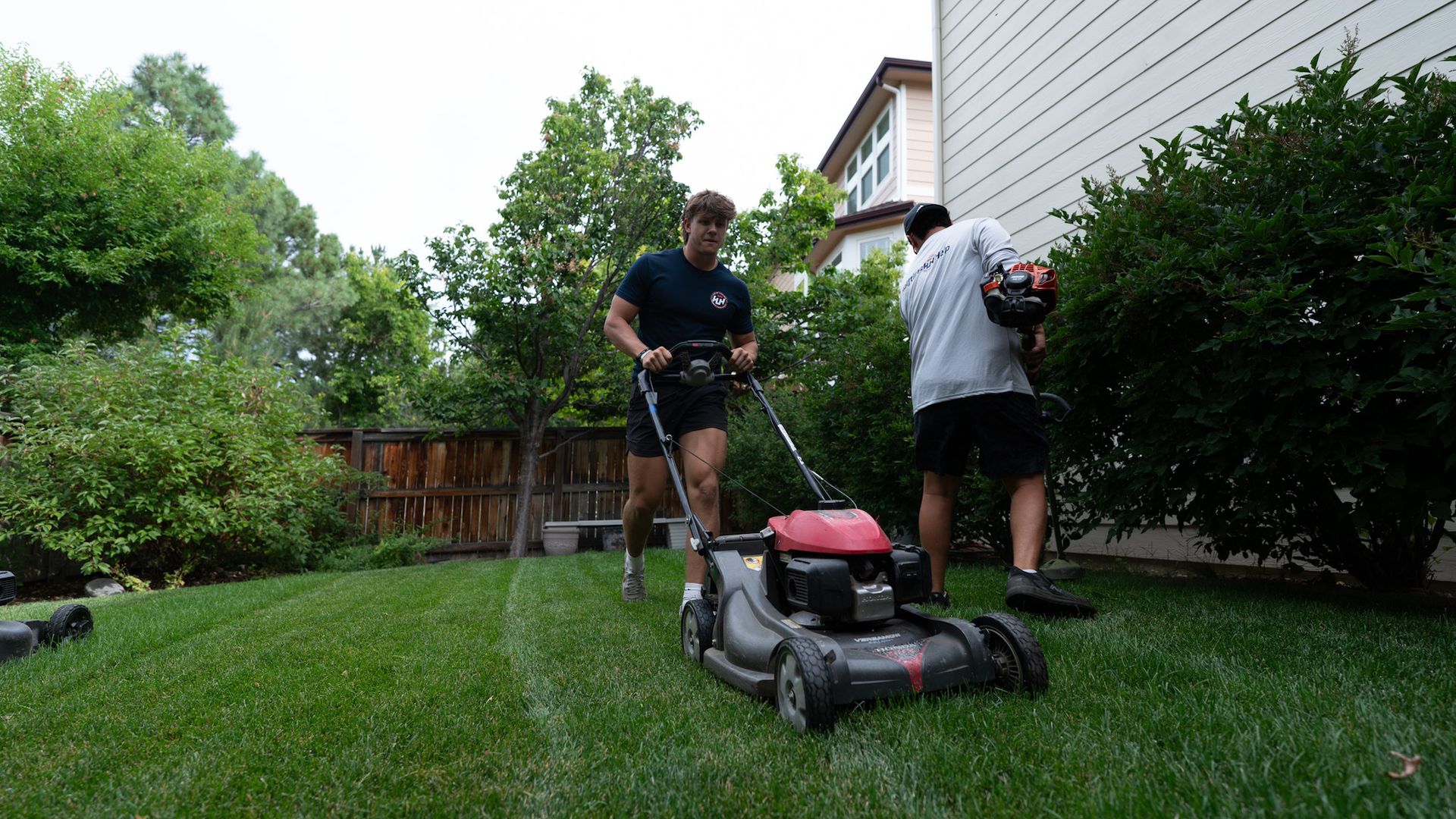 A man using a lawn mower and a man using a grass cutter.