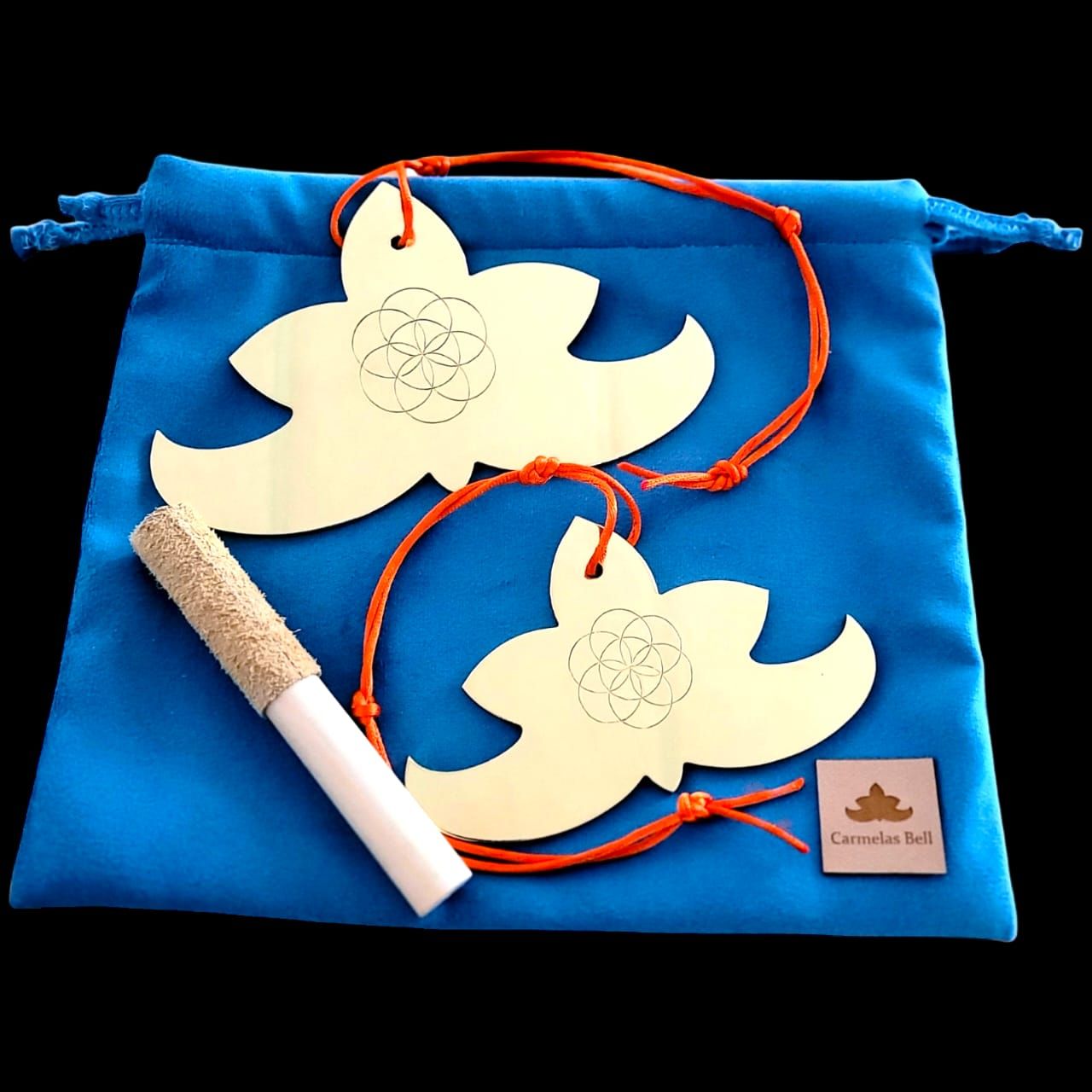 Dos campanillas doradas con forma de pétalo y cuerda naranja, apoyadas sobre una bolsa azul y con un percutor.